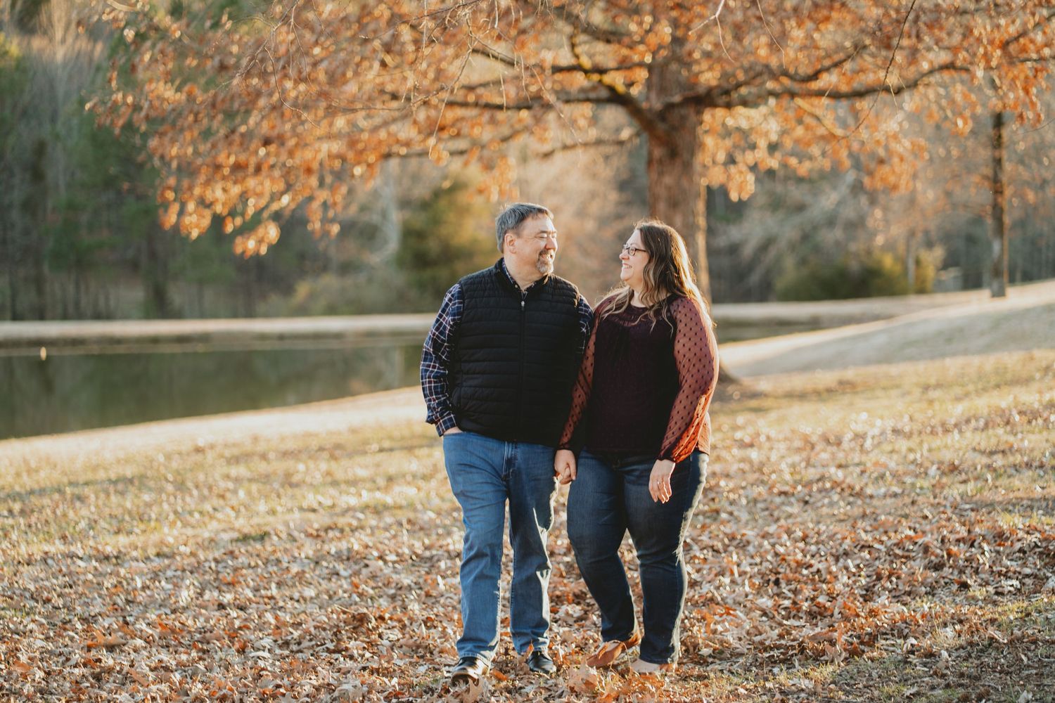 Couple standing together among autumn leaves near a peaceful pond.
