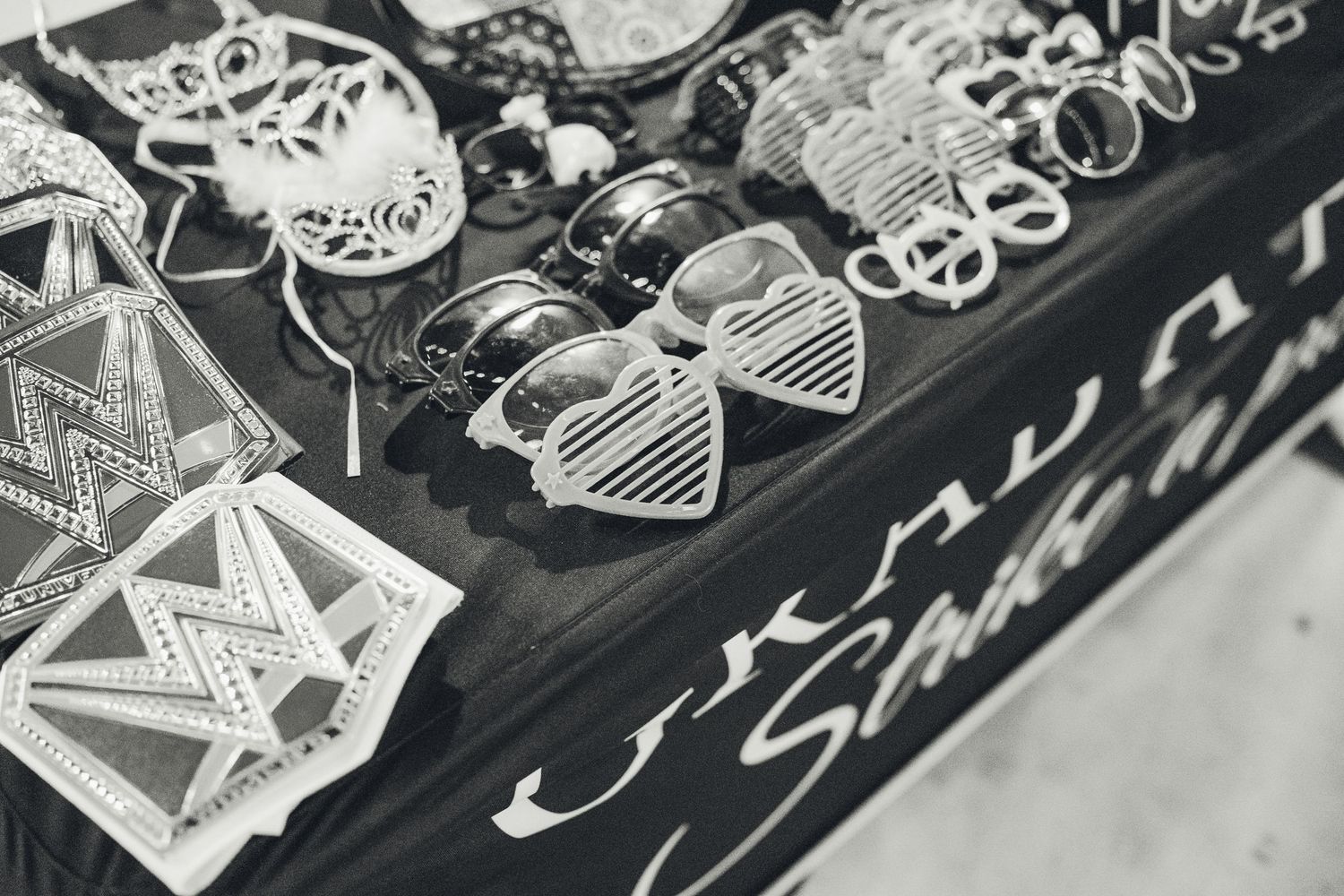 Black and white photo of heart-shaped sunglasses and accessories displayed on a market stall table.