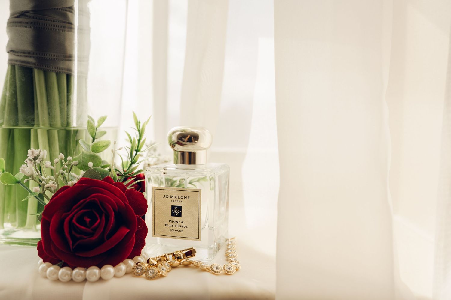 Elegant wedding flat lay featuring a red rose, pearl necklace, and Jo Malone perfume bottle.