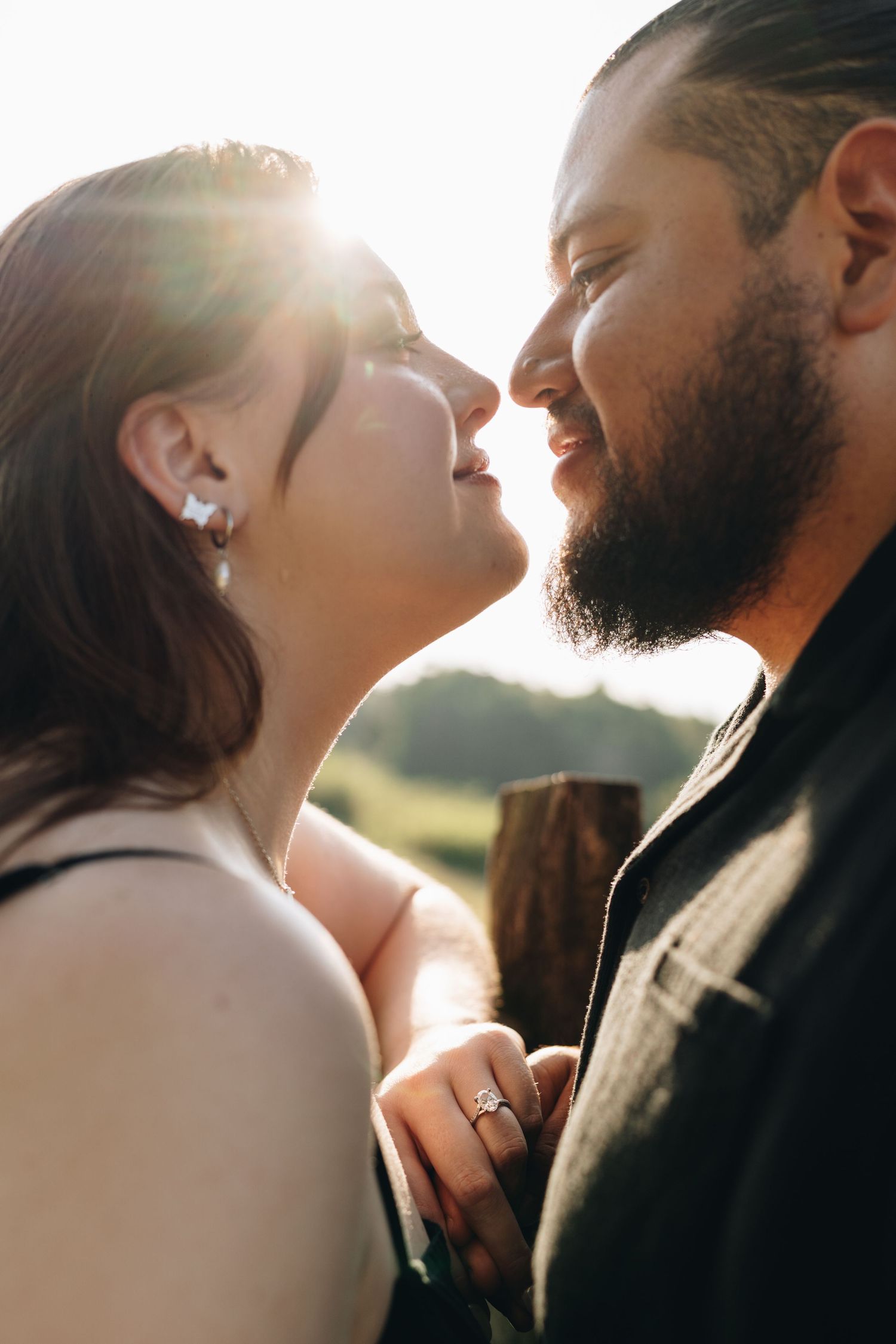Intimate close-up of engaged couple almost kissing in golden sunlight, woman wearing a diamond ring.