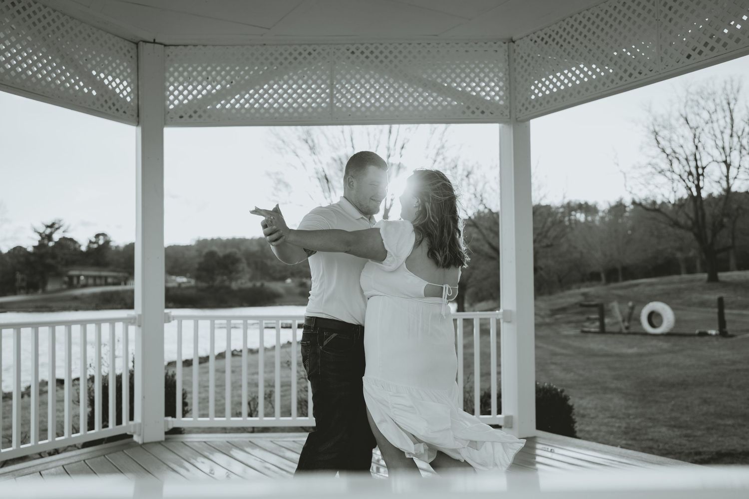 Black and white photo of couple dancing romantically in a white gazebo during engagement session.