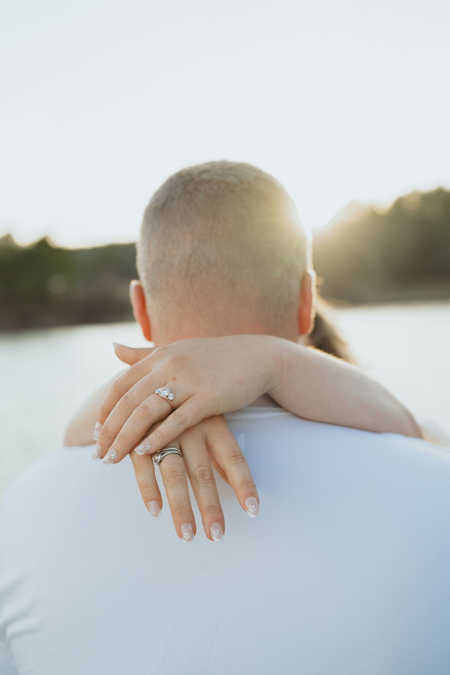 Close-up of womans hands showing engagement ring and wedding band wrapped around mans shoulders.
