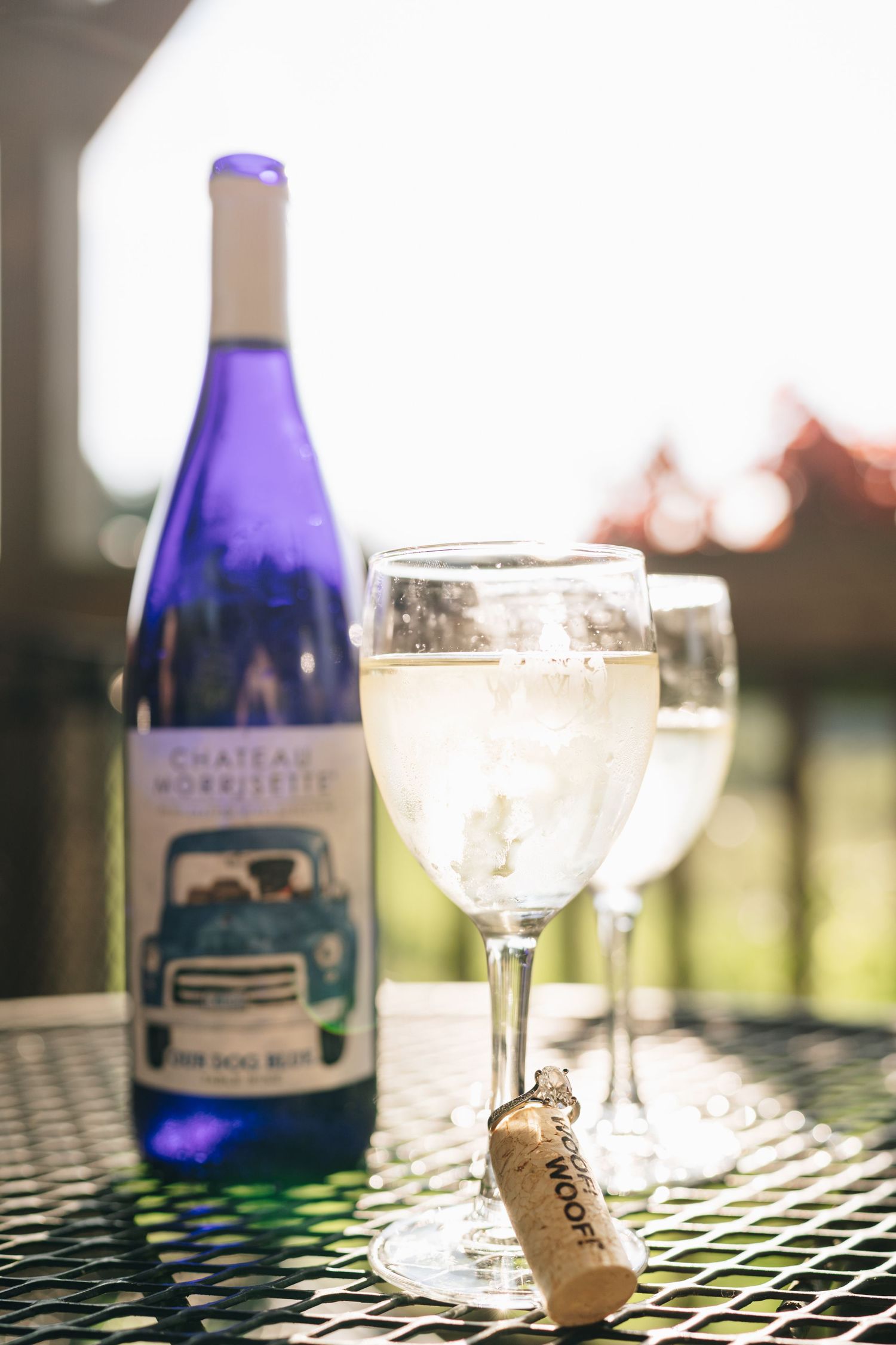 Blue bottle of Chateau Morrisette wine with two glasses on an outdoor patio table in sunlight.