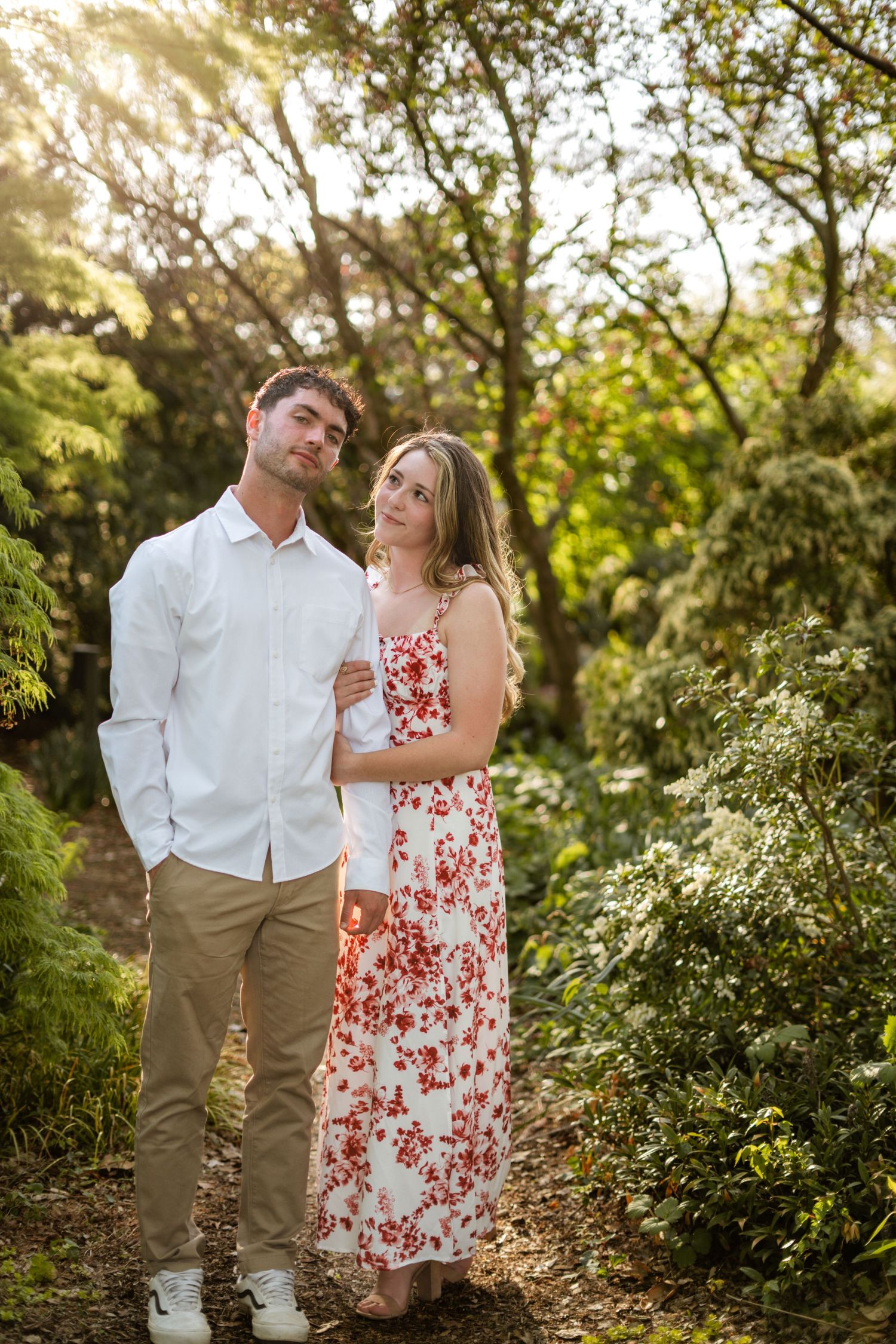 Couple embracing in sunlit garden, woman in floral dress holding mans arm.