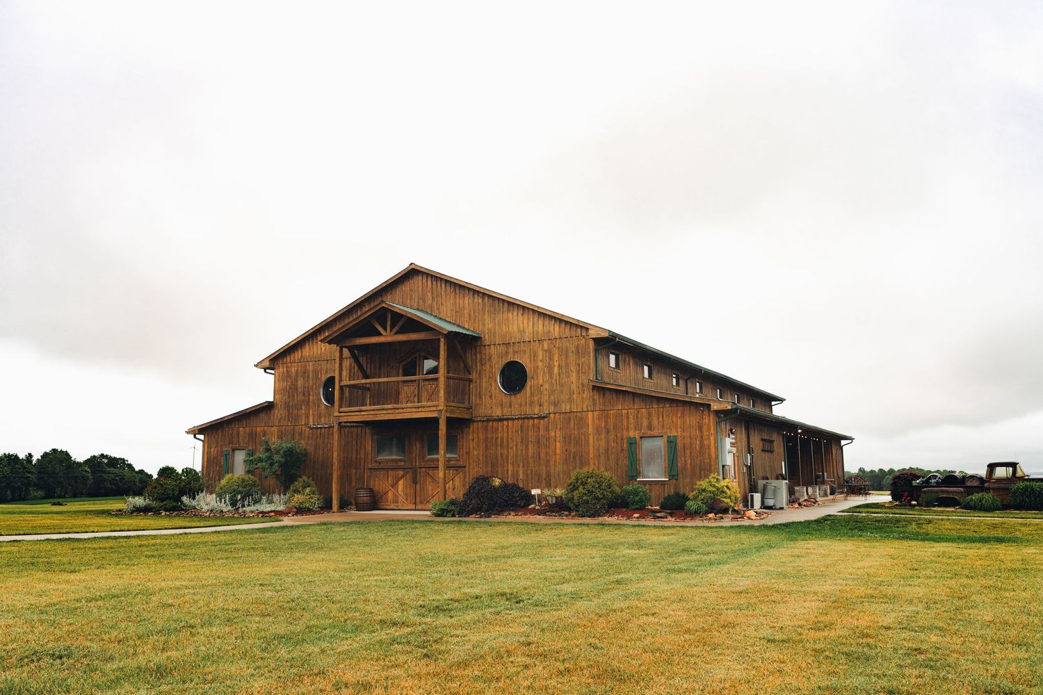 Large rustic wooden barn venue surrounded by green lawns under overcast skies, ideal for country weddings.