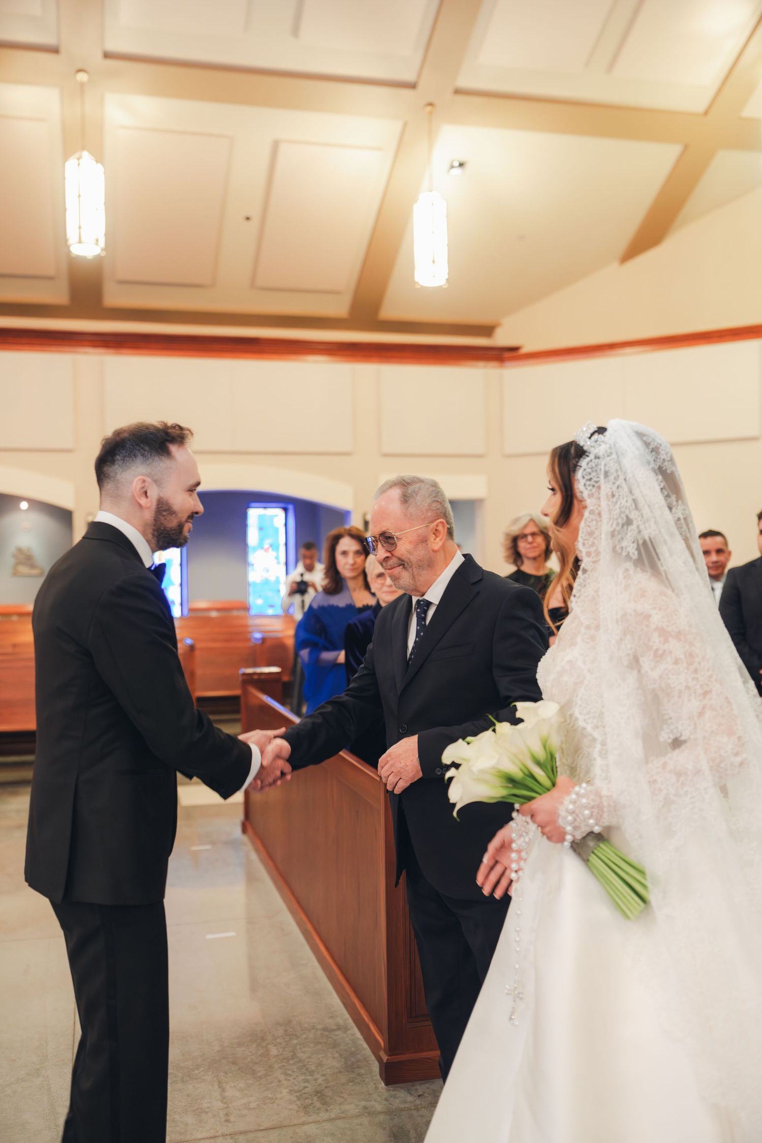 Groom shakes hand with brides father during church wedding ceremony handoff at altar.