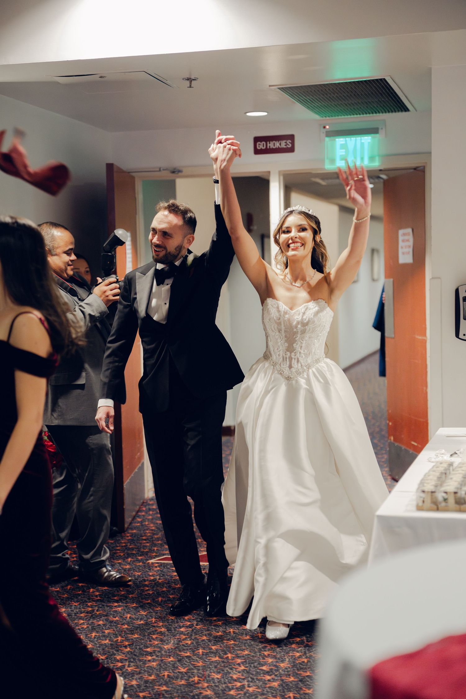 Joyful bride and groom making grand entrance into wedding reception hall with guests celebrating around them.