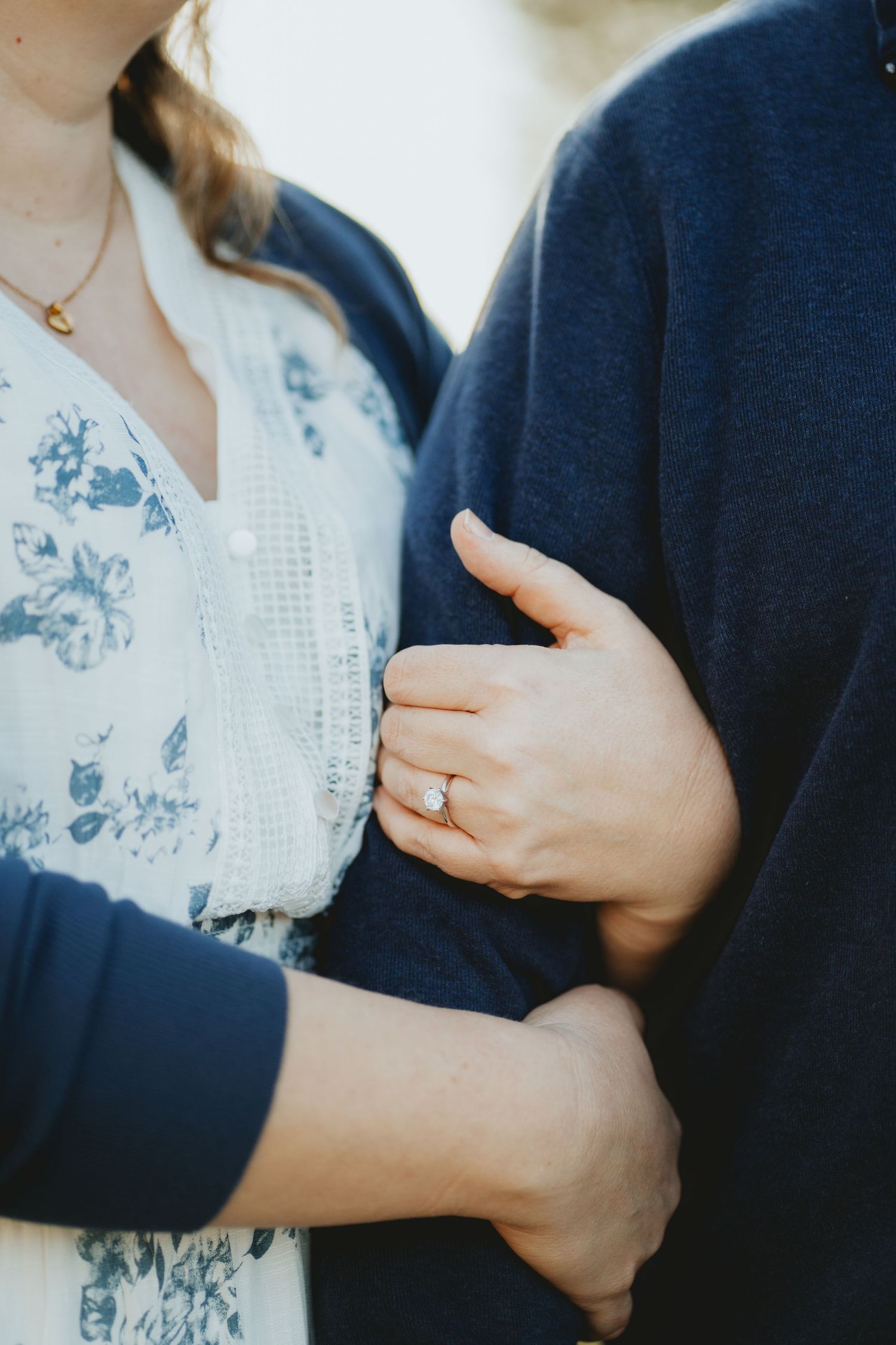 Close-up of a woman's hand with an engagement ring resting on a man's arm.
