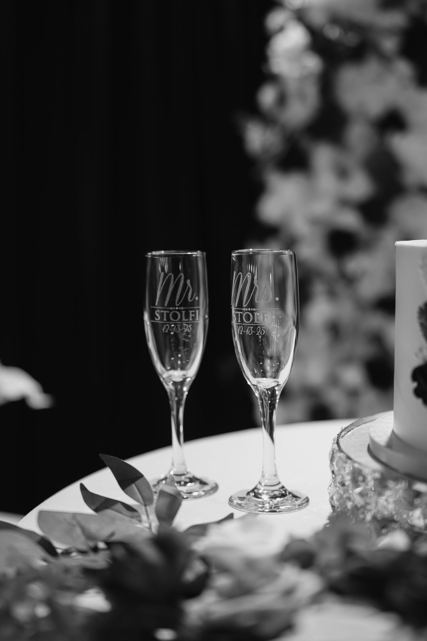 Black and white photo of personalized Mr. and Mrs. Stolfi engraved champagne flutes on wedding table.