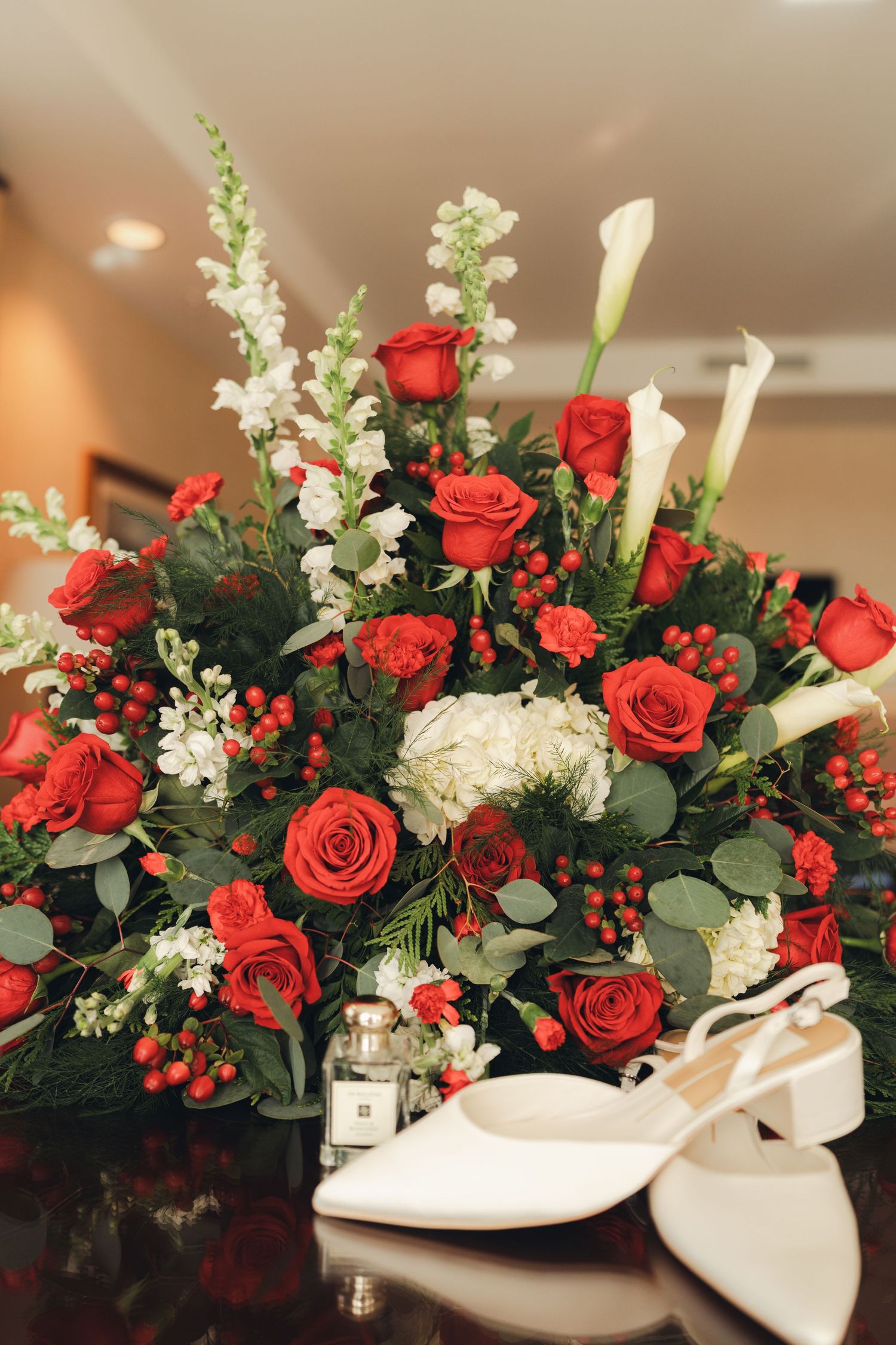 Elegant wedding bouquet of red roses and white calla lilies with bridal heels.