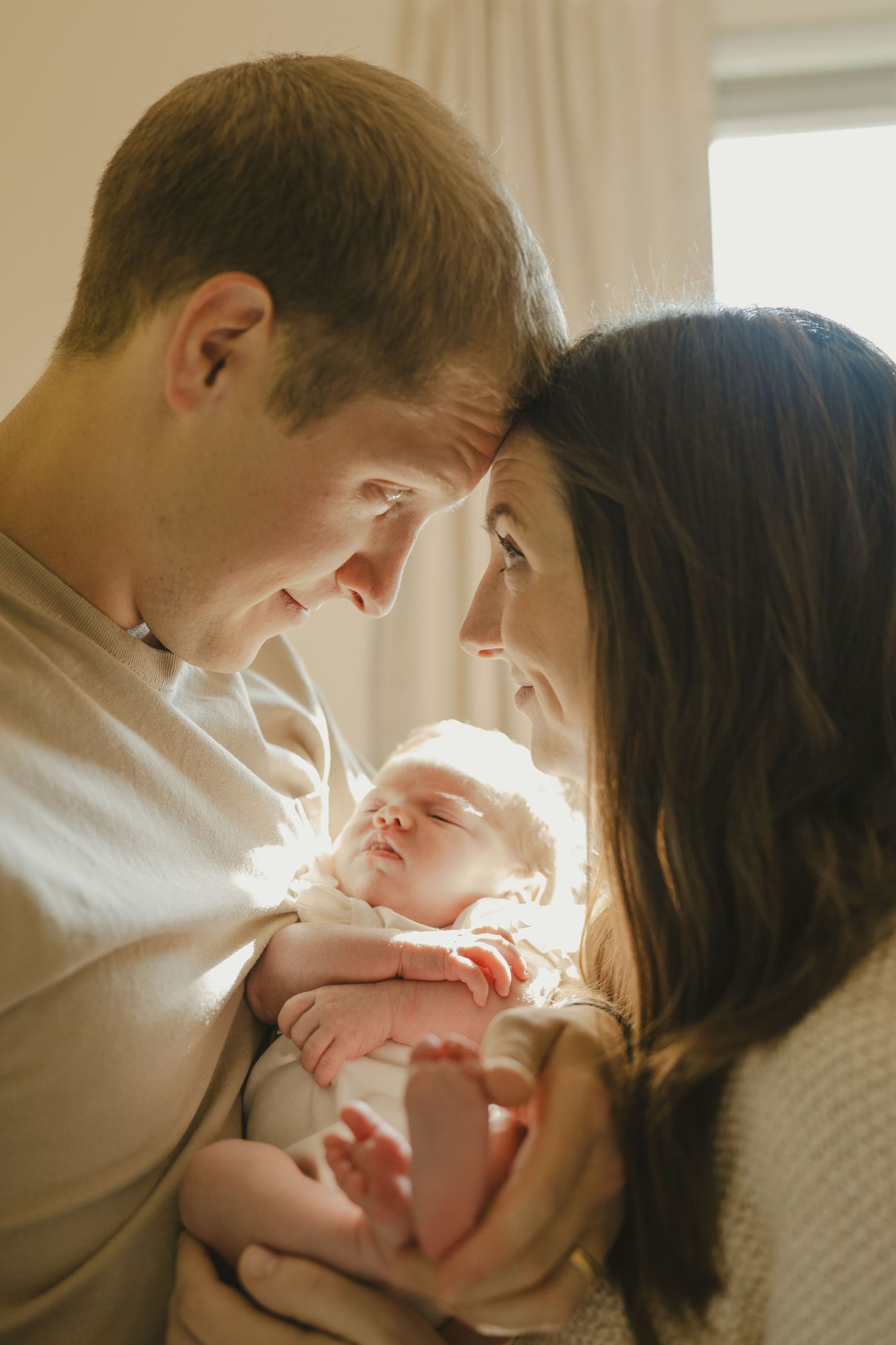 Loving parents touching foreheads together while cradling their peaceful sleeping newborn baby.