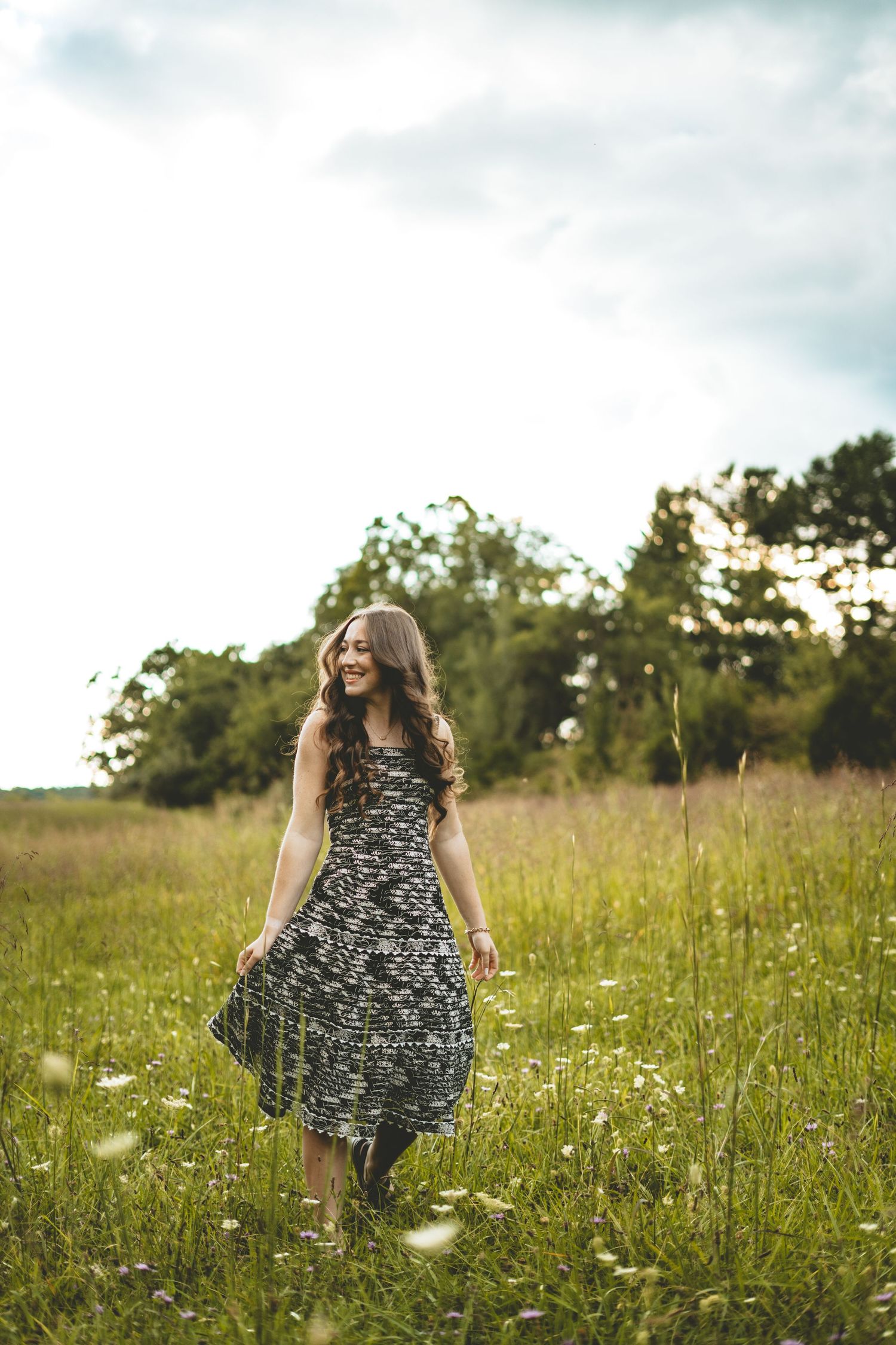 Happy young woman in floral dress walking through a green meadow on a sunny day.