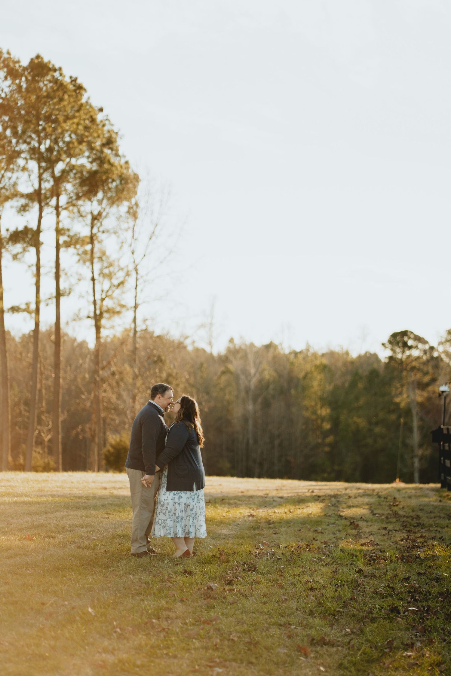 Couple standing close together in a golden sunlit meadow at sunset.