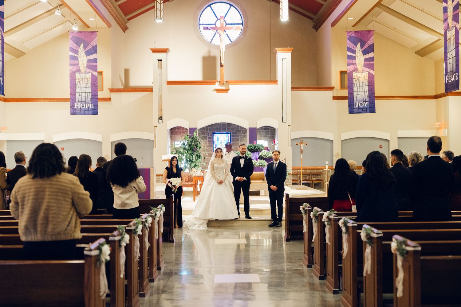 Wide shot of bride and groom walking down church aisle with guests seated in pews.