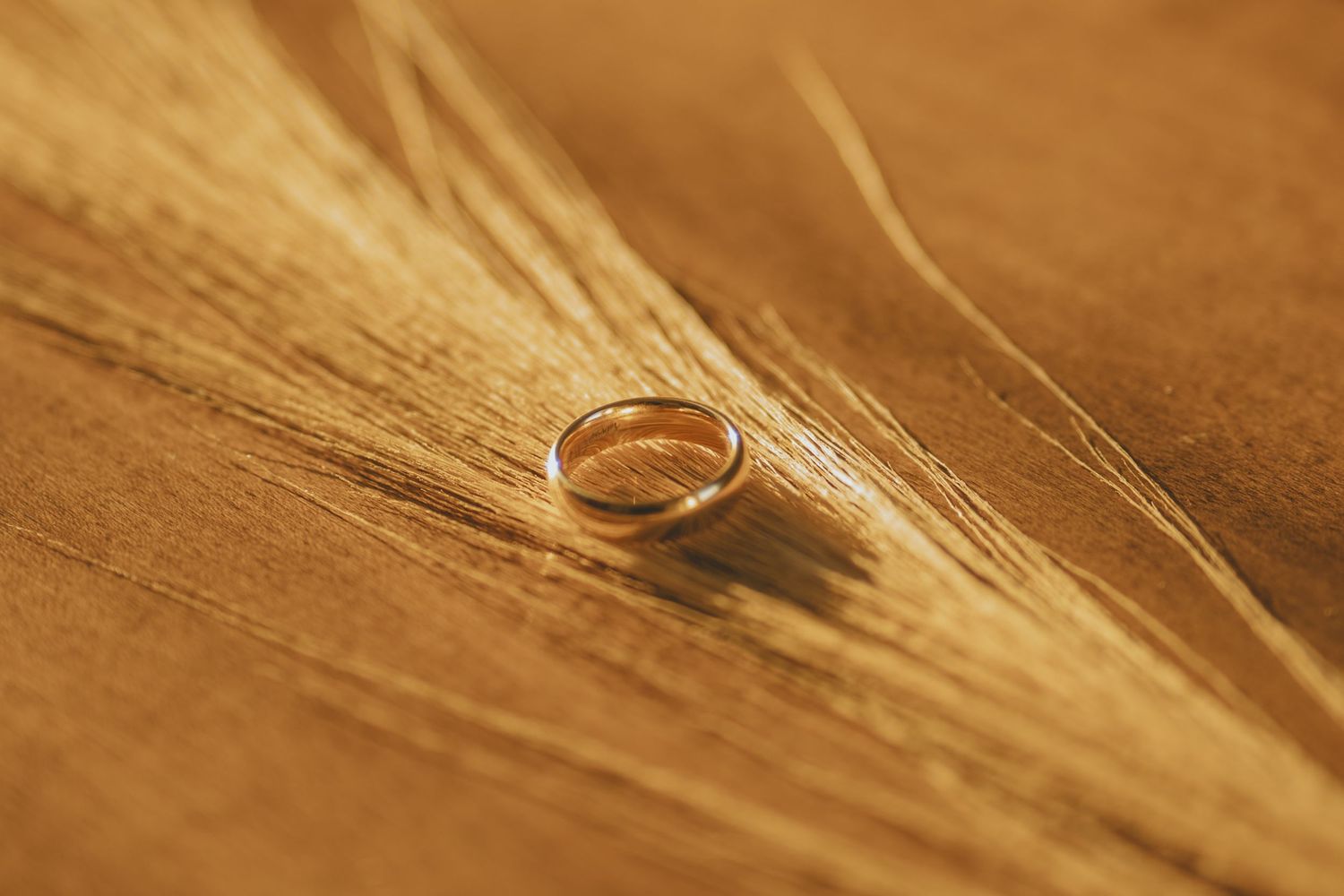 Gold wedding band resting on golden textured fabric in warm autumn light.