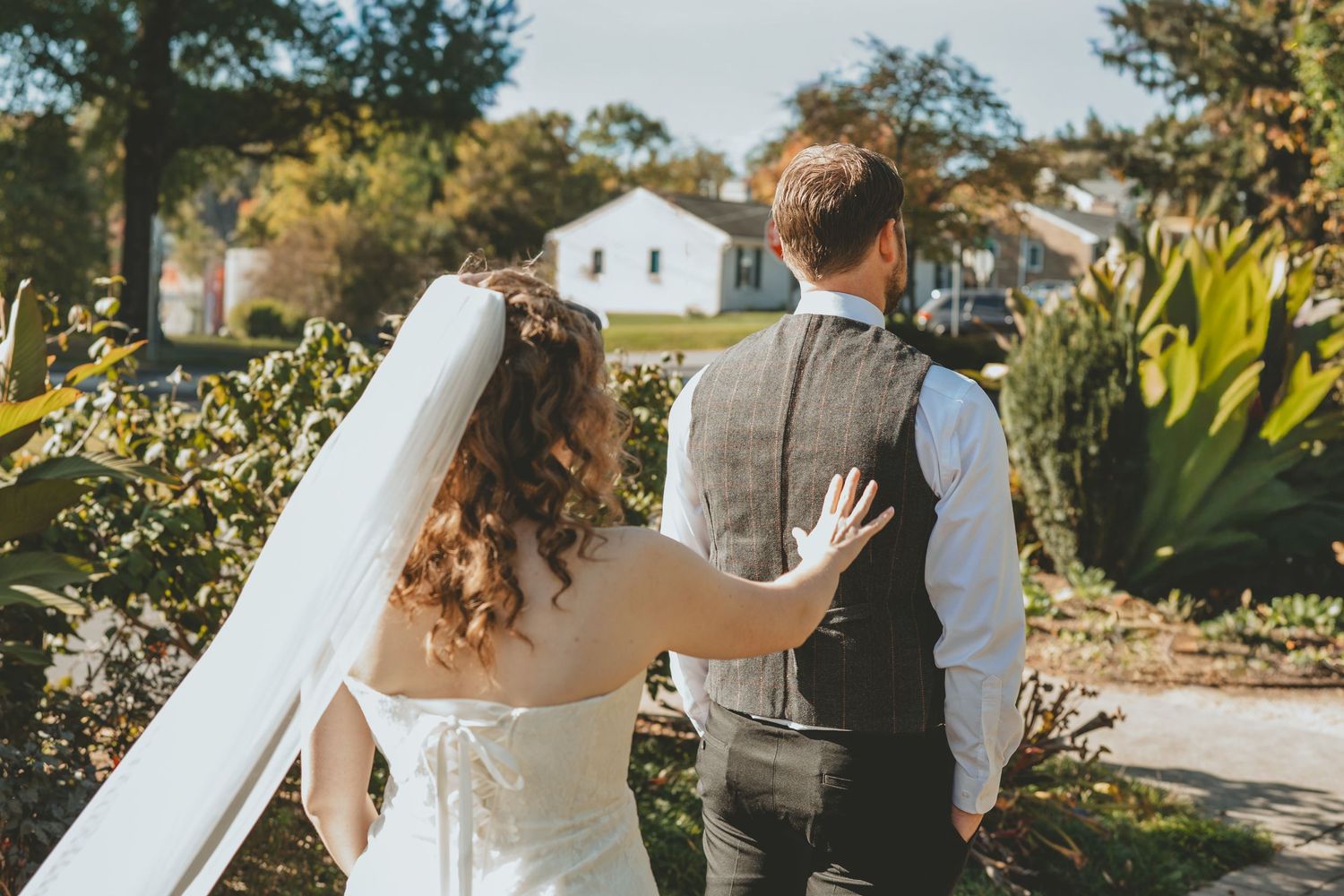 Bride and groom walking hand in hand through lush garden on wedding day.