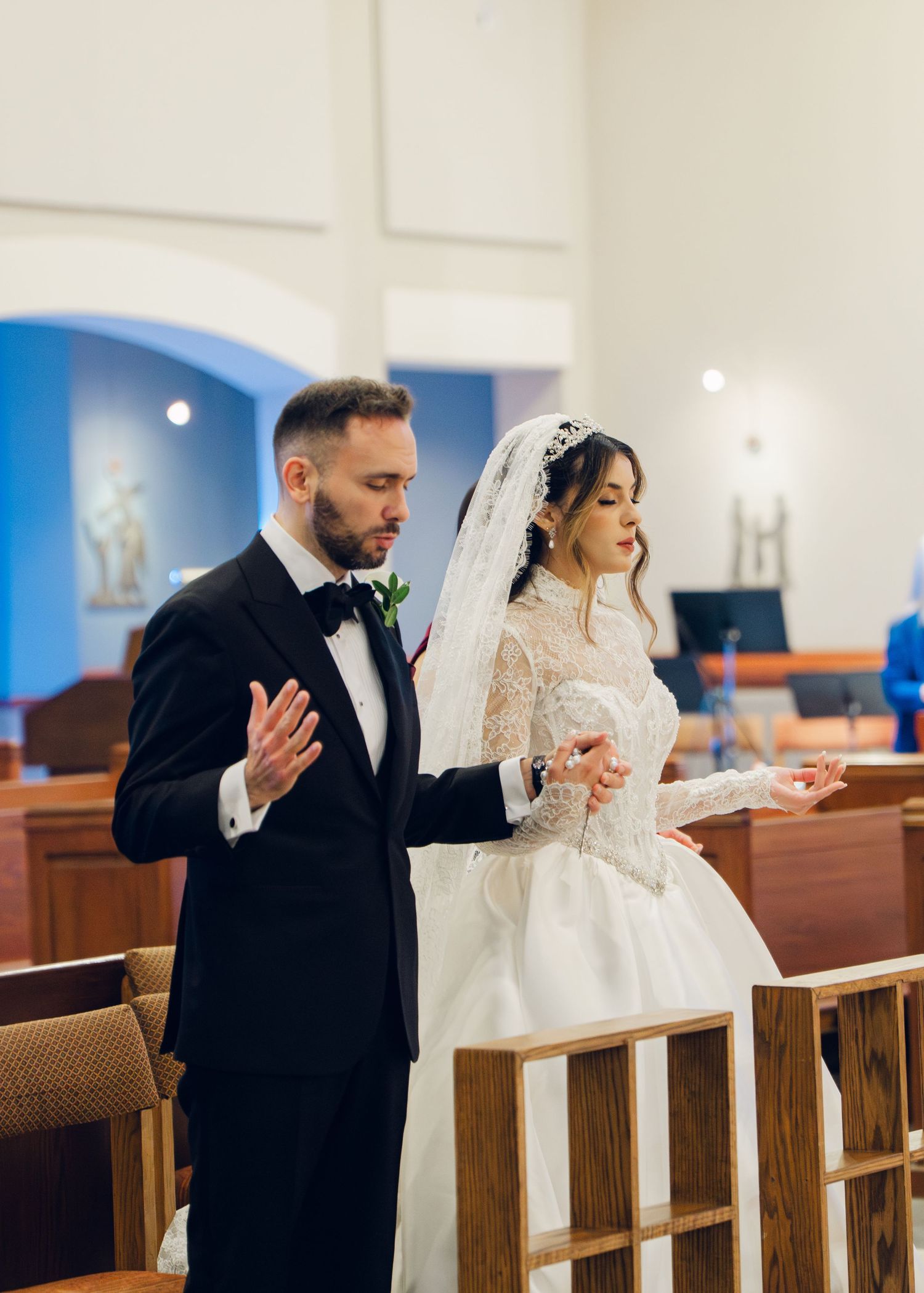 Bride and groom pray together with open hands during Catholic church wedding ceremony.