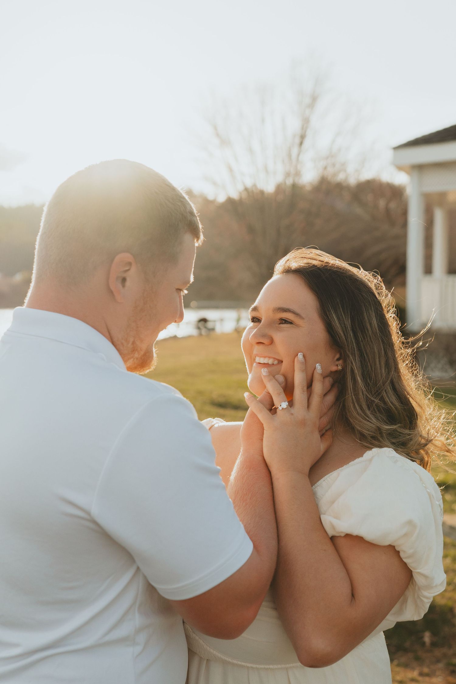 Smiling bride-to-be being held by her fiance in warm sunset light showing her engagement ring.