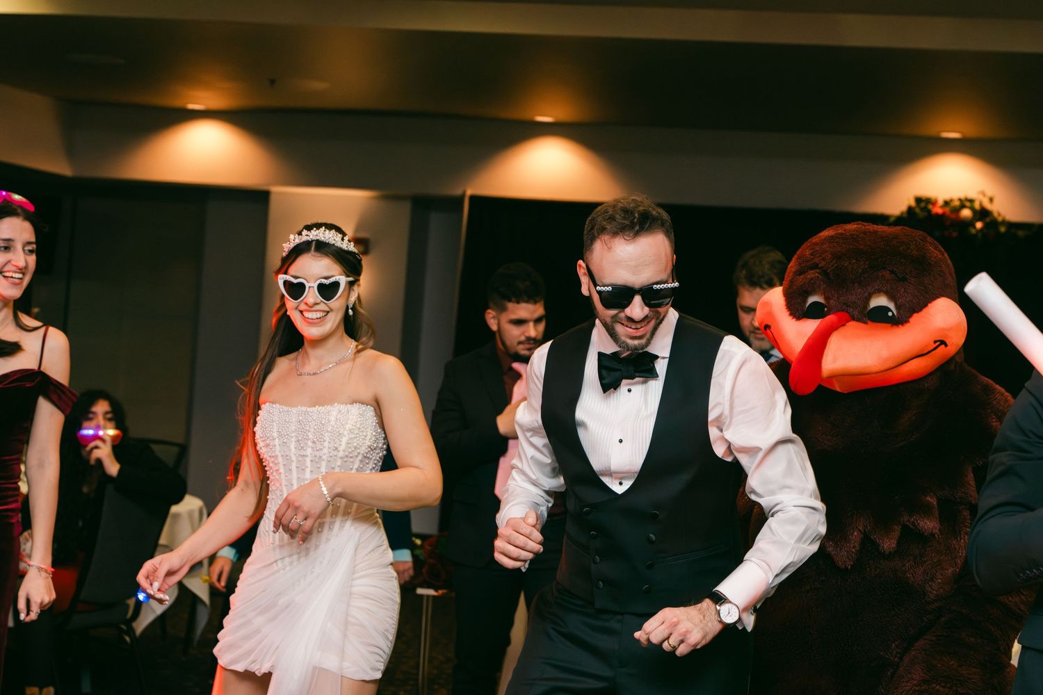 Bride and groom dancing with mascot at fun wedding reception party.