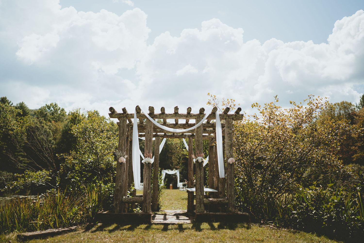 Rustic wooden pergola draped with white fabric serves as an elegant outdoor wedding ceremony arch.