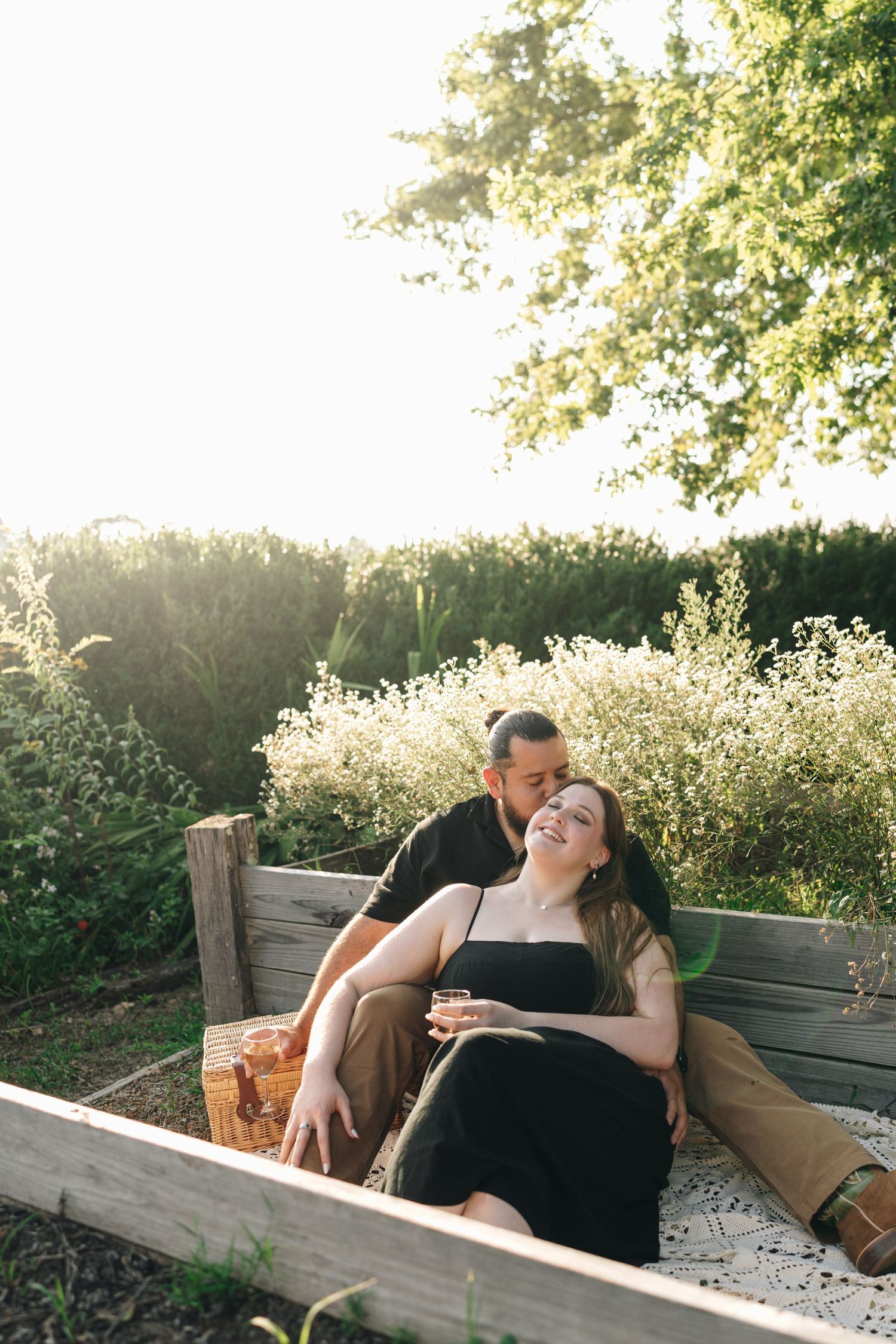 Couple sitting together in a garden laughing and sharing a tender moment in golden sunlight.
