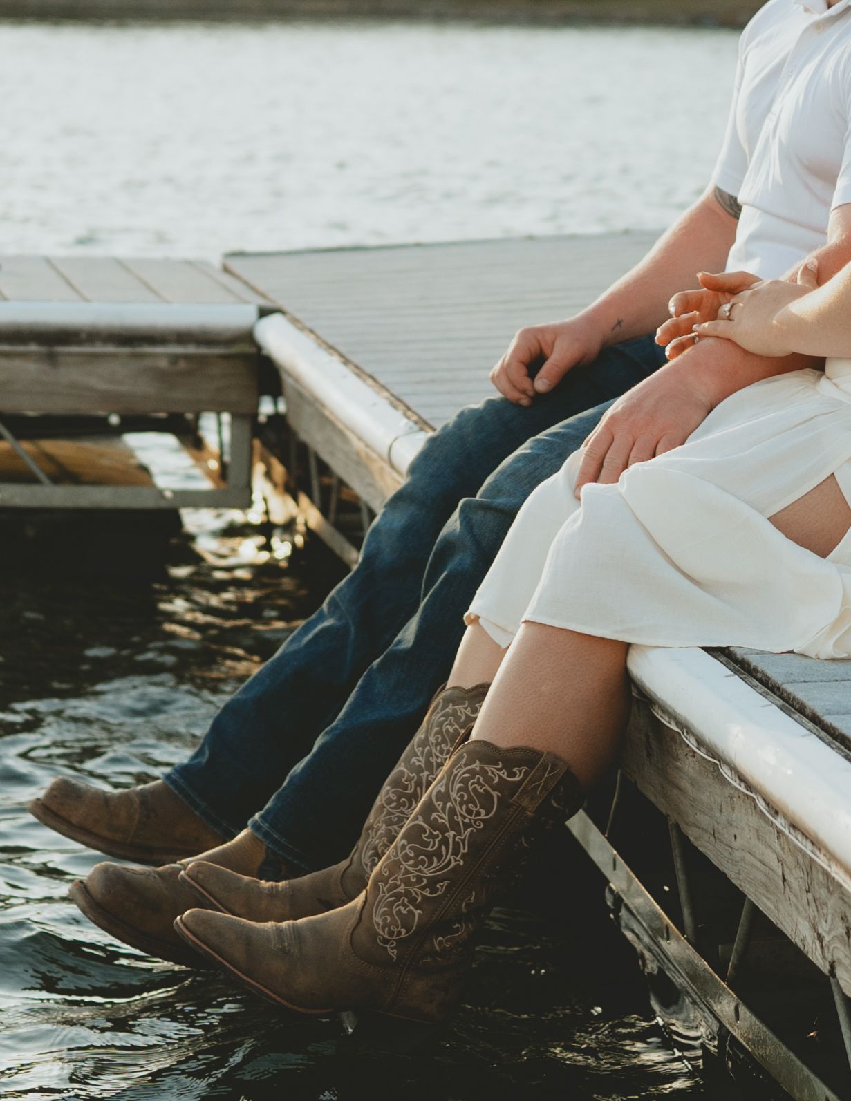 Close-up of couple sitting on a dock over water wearing cowboy boots and jeans.