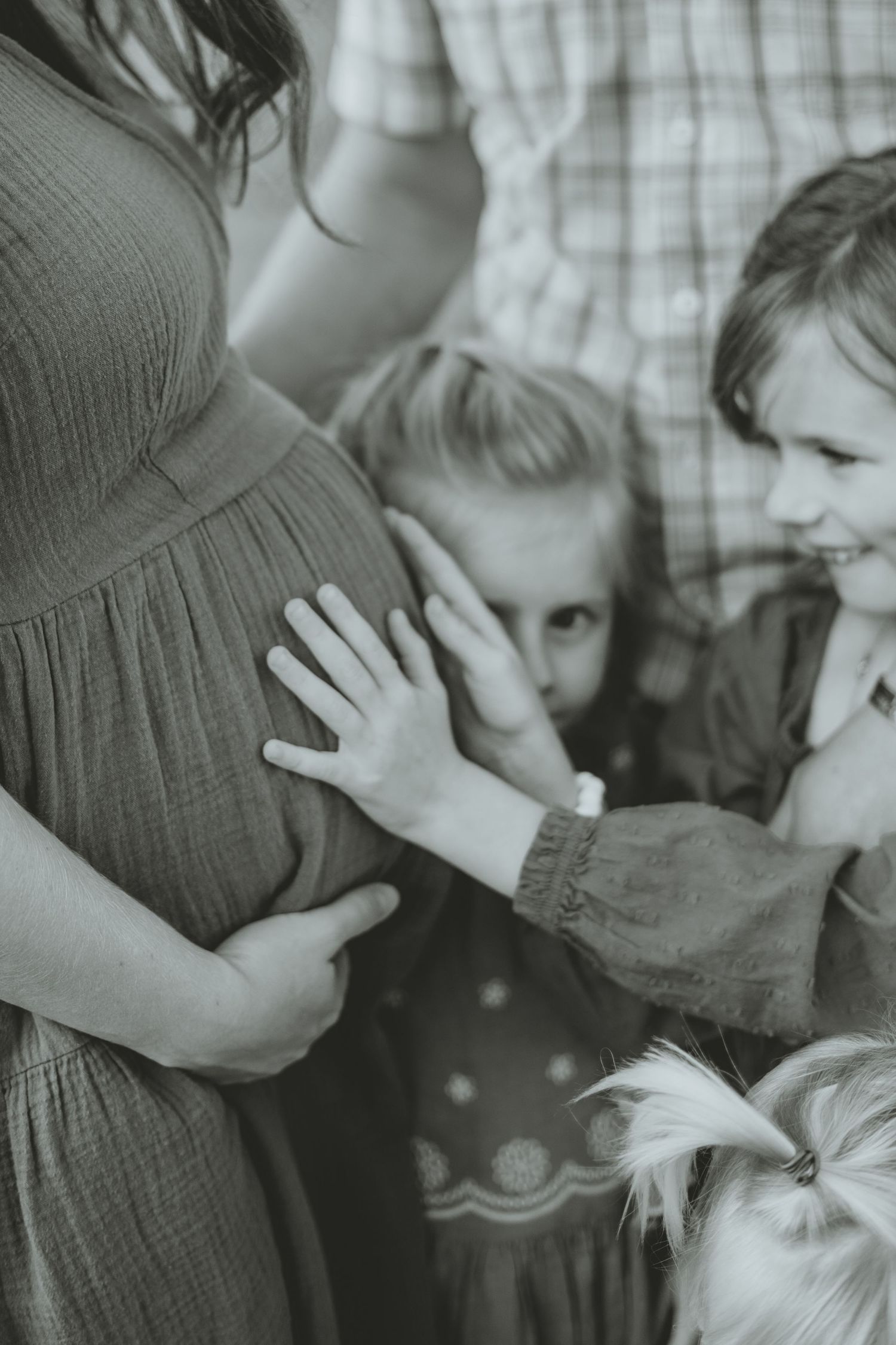 Black and white photo of children touching pregnant mothers belly in tender family maternity moment.