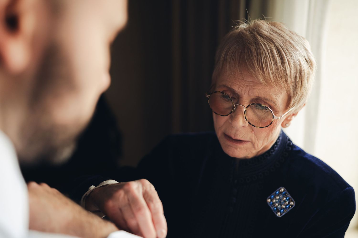 Elderly woman examining a man's wrist watch during wedding preparations.