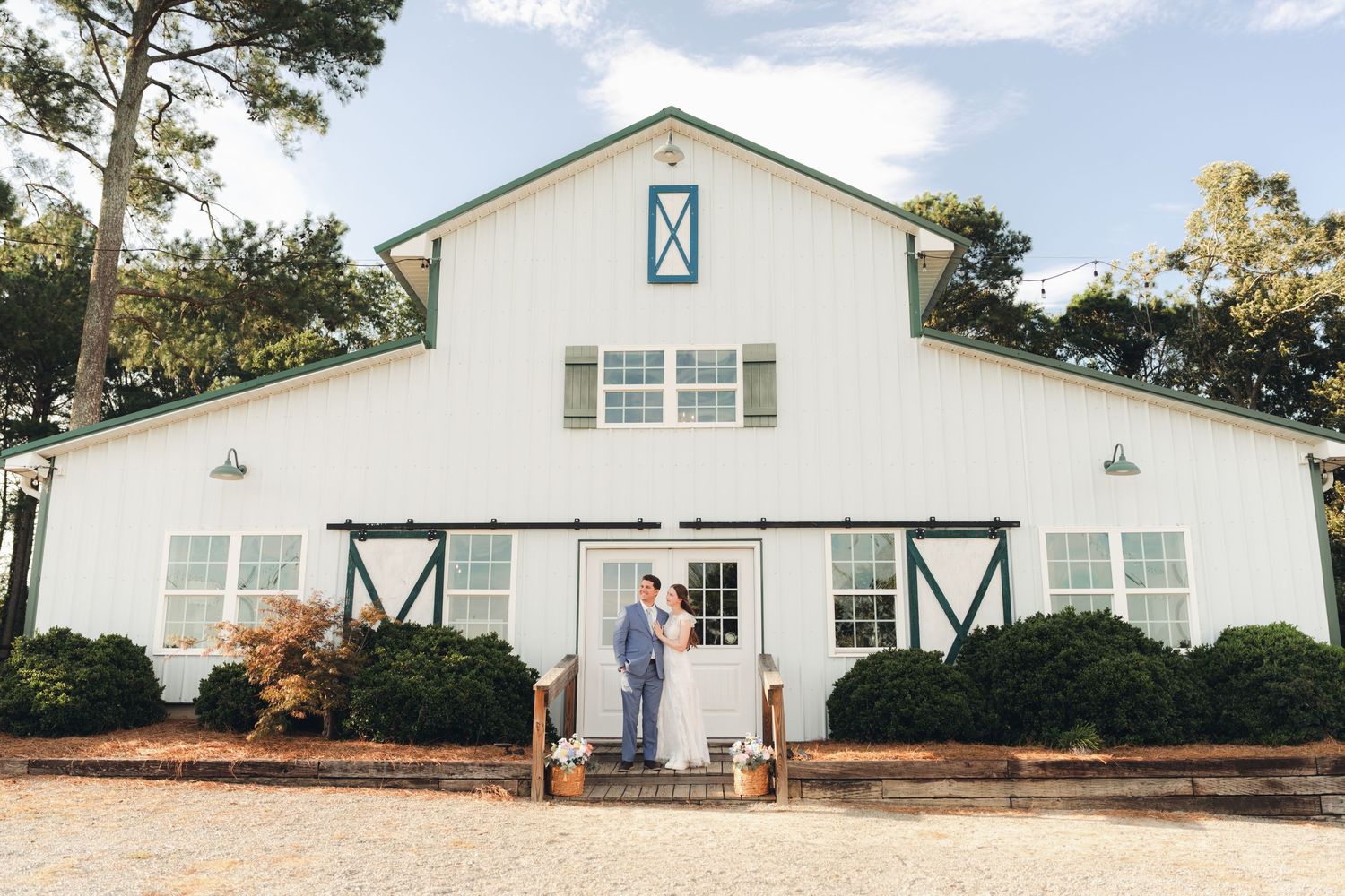 Couple embracing at entrance of white barn wedding venue with green accents and sliding doors.