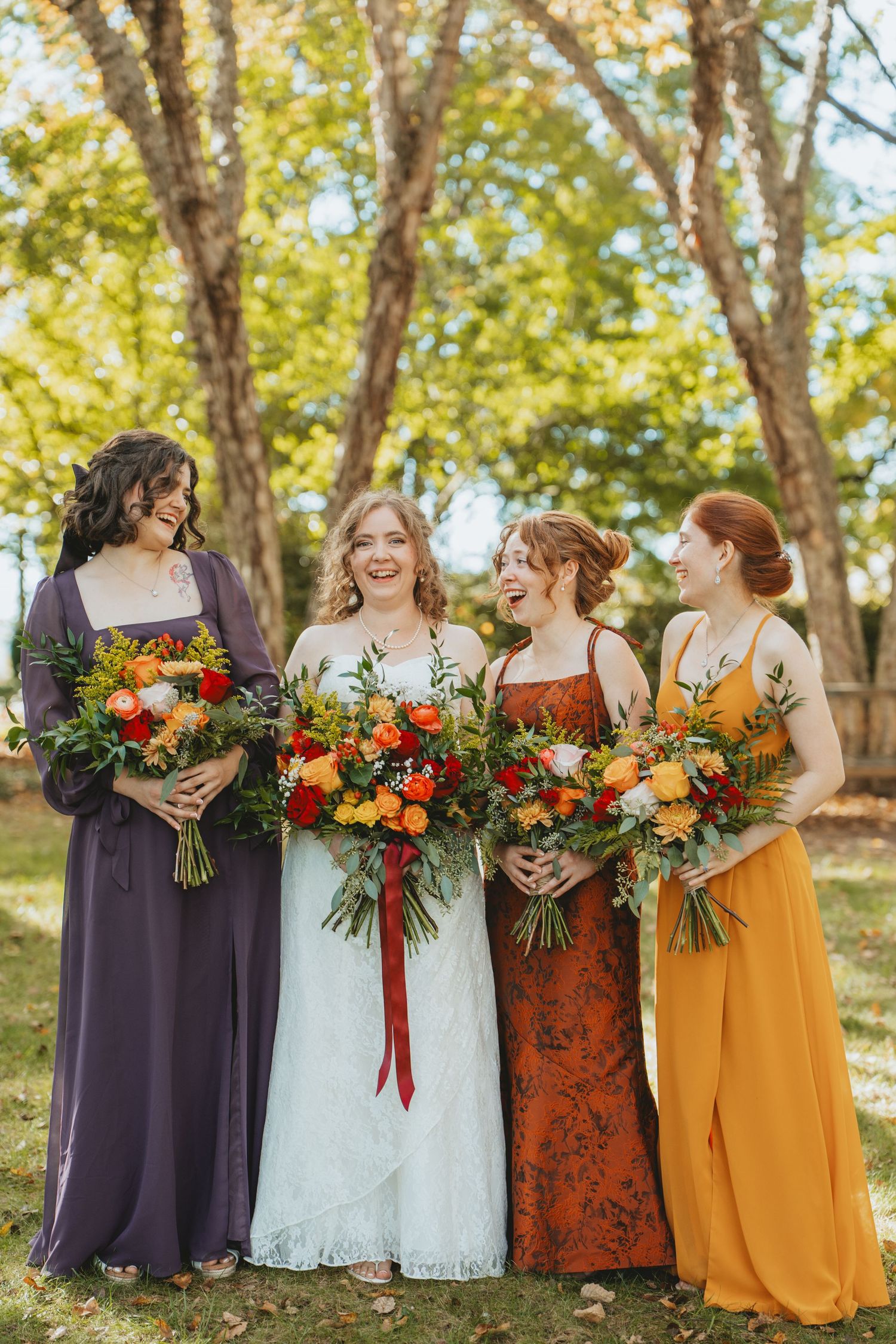 Bride with three bridesmaids in purple, rust, and mustard dresses holding fall bouquets.
