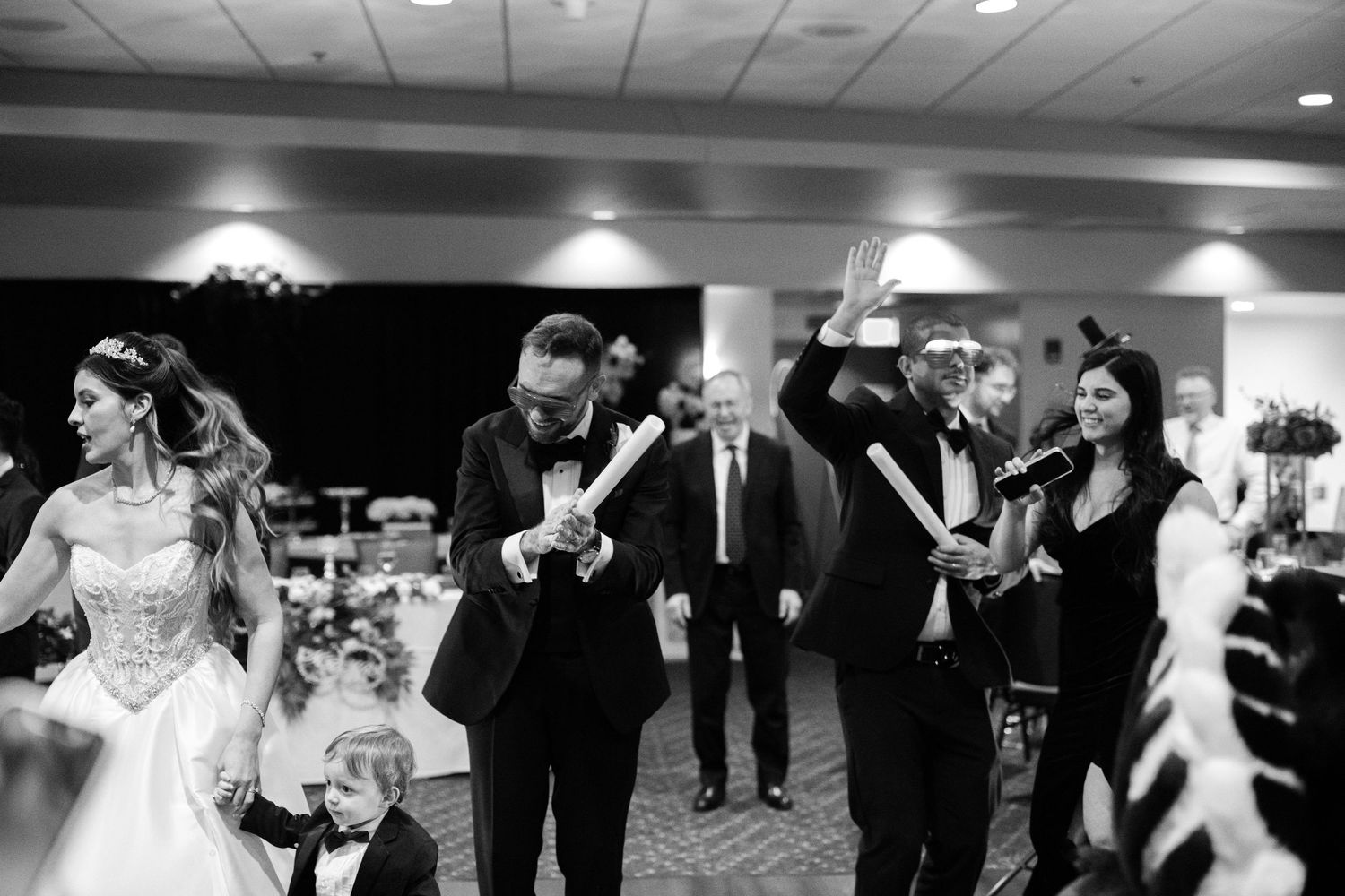 Bride and groom walk with wedding party holding scrolls at elegant black and white reception.