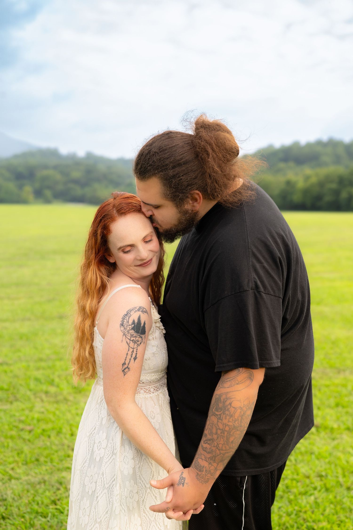 Tattooed couple holding hands and sharing a tender moment in a lush green meadow outdoors.