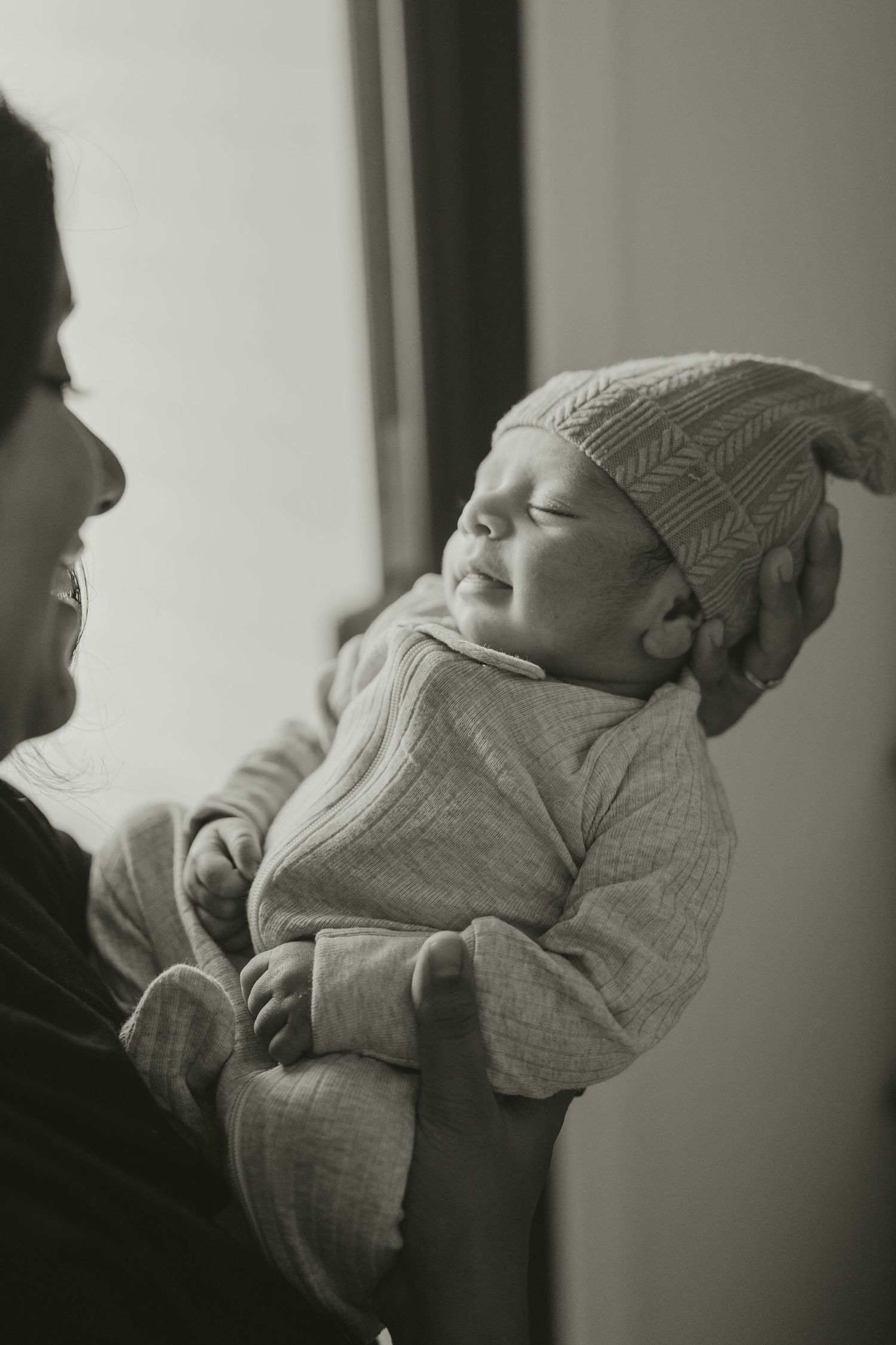 Monochrome image of a parent holding a sleeping newborn dressed in a cozy knit hat.