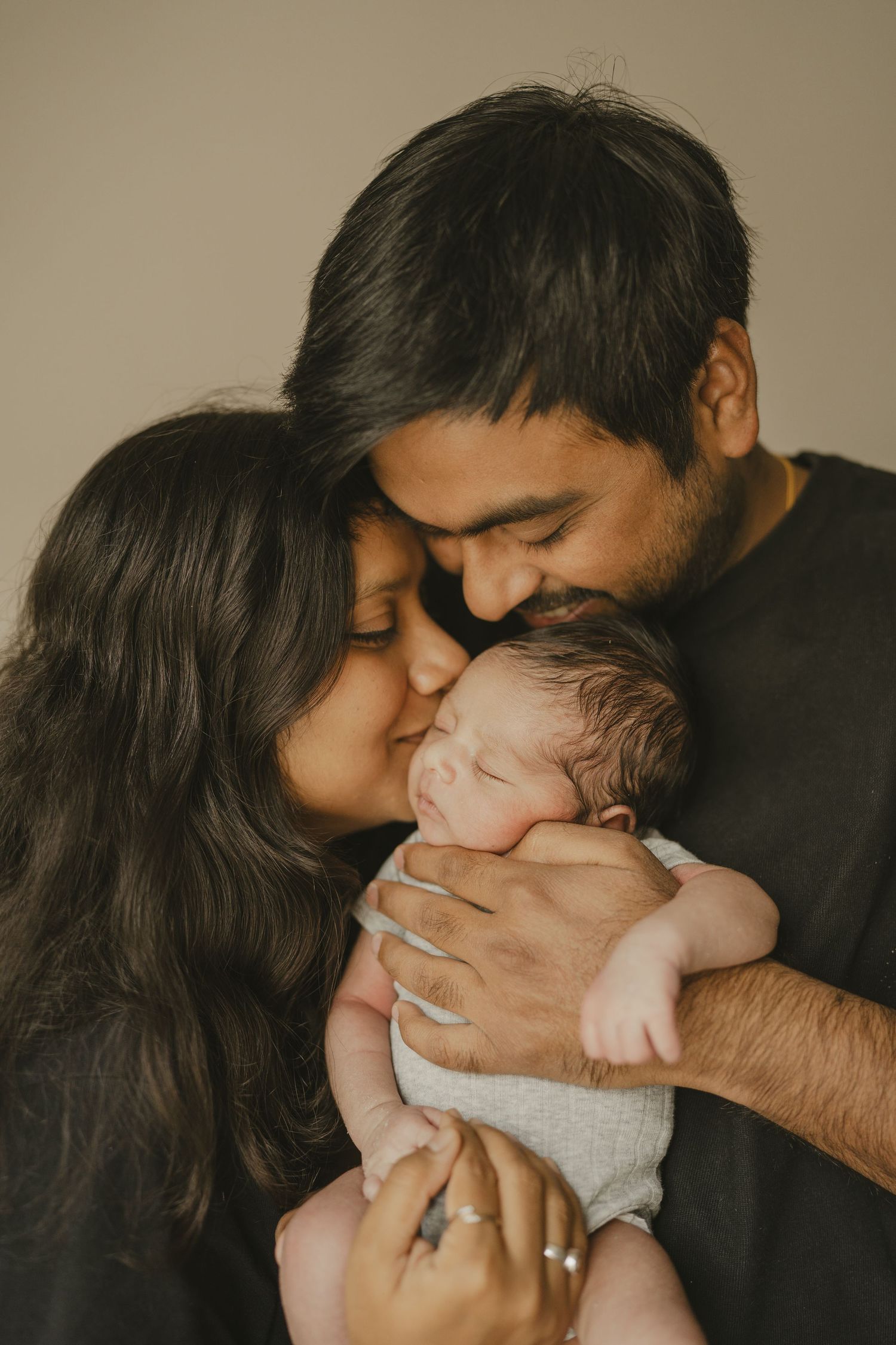 Parents tenderly kissing their sleeping newborn baby held gently in dads arms.