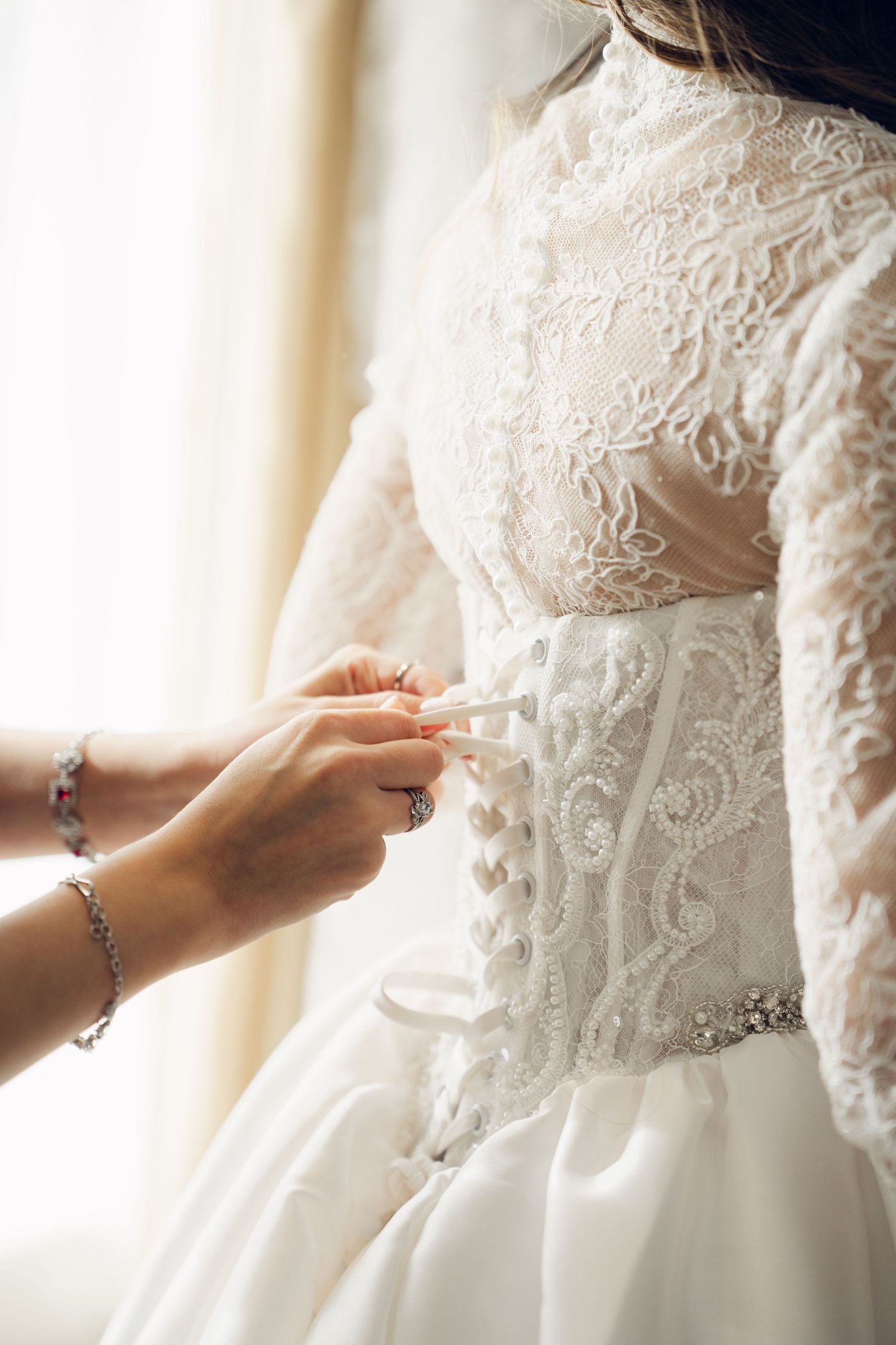 Bridesmaid lacing up back of brides lace corset wedding gown.