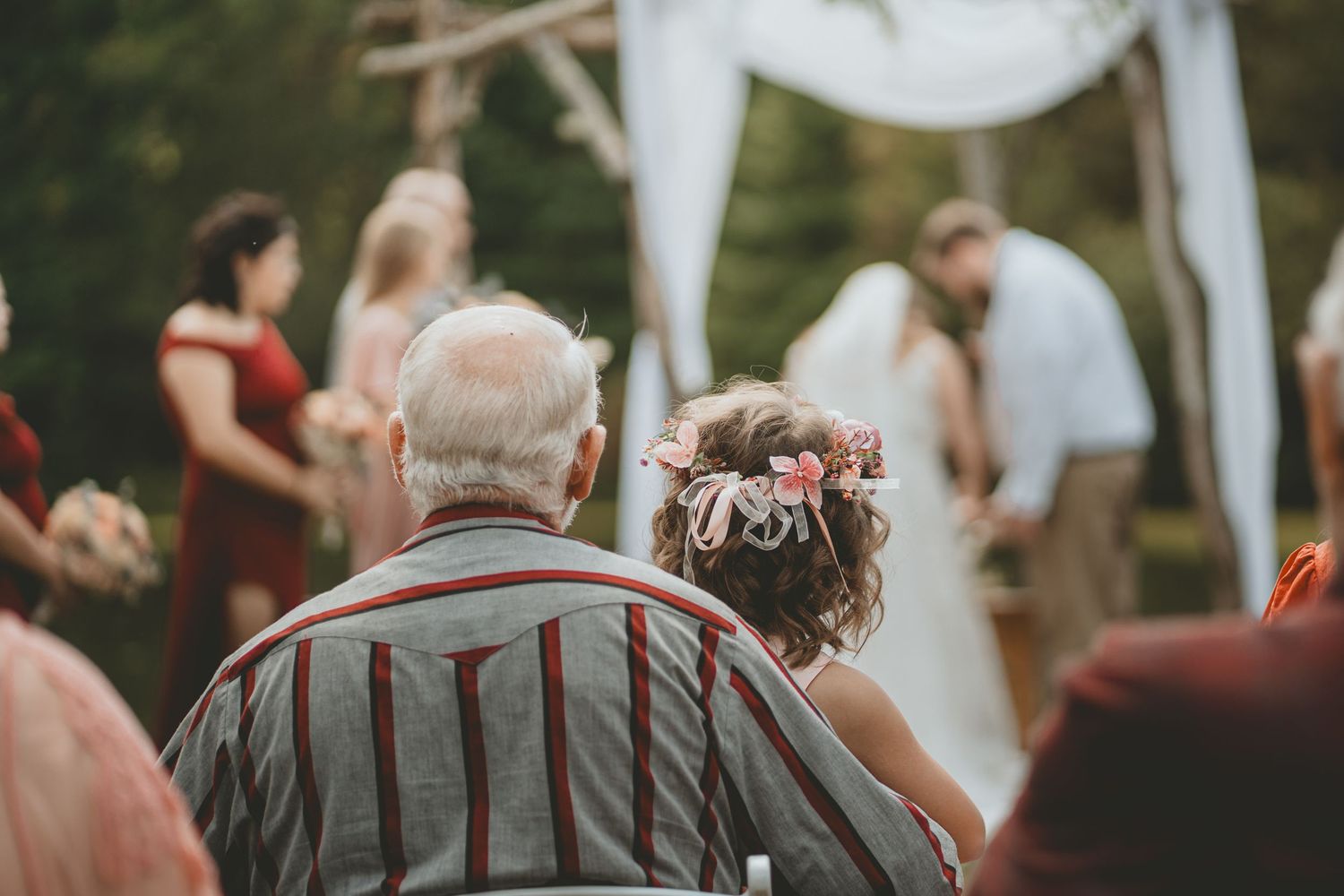 Wedding guests seated outdoors watch couple exchange vows at a rustic garden ceremony altar.