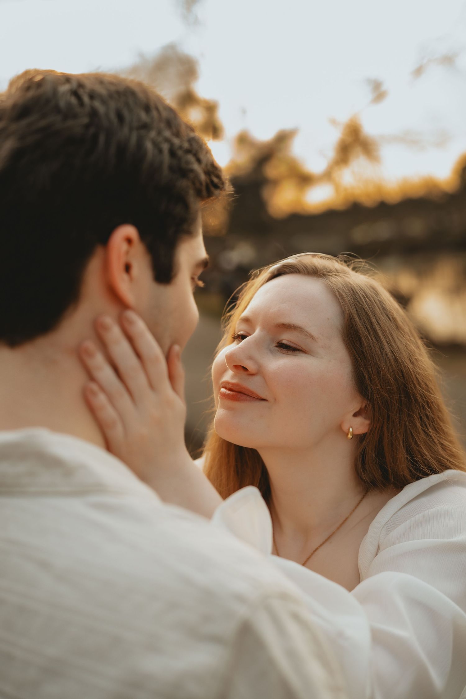 Close-up of a smiling woman with red hair gazing at her partner during golden hour outdoors.