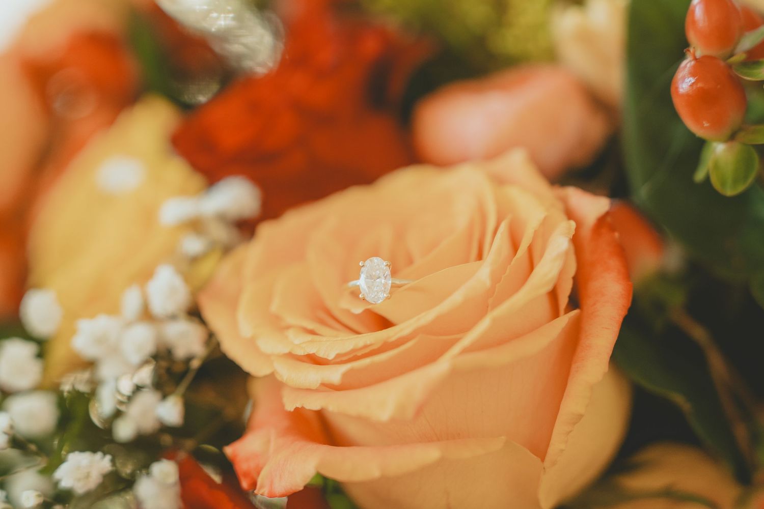 Diamond engagement ring resting elegantly on a peach rose in a bridal bouquet.