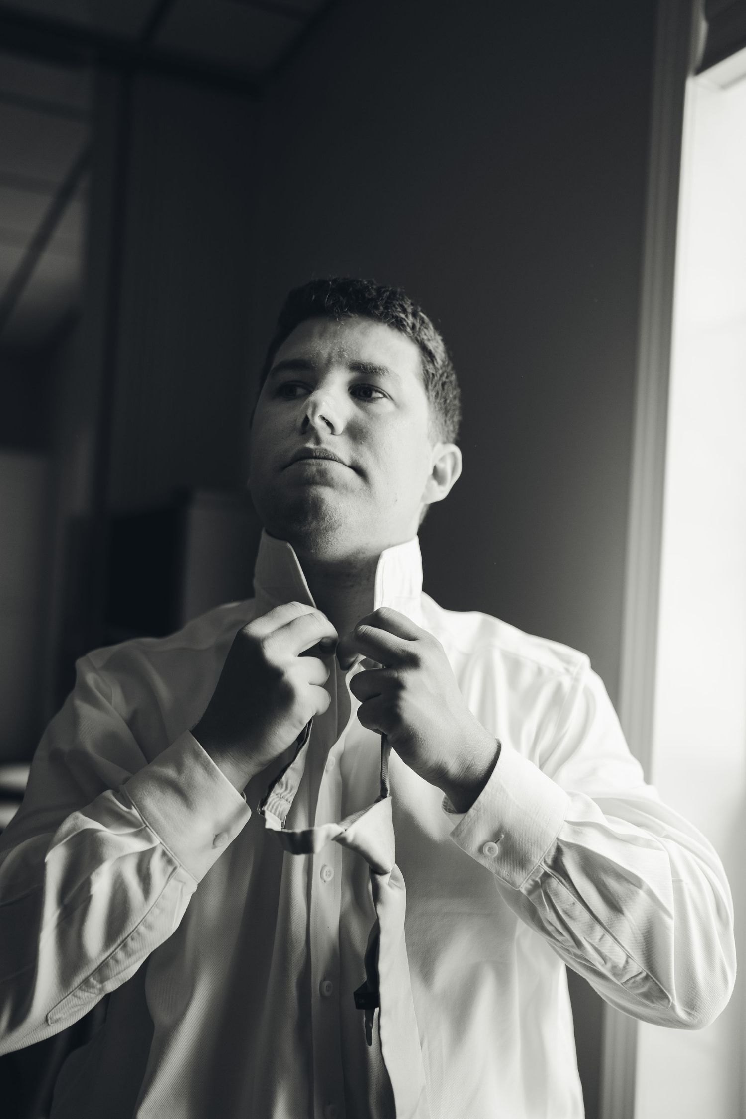 Black and white photo of a groom adjusting his tie while getting ready for his wedding day.
