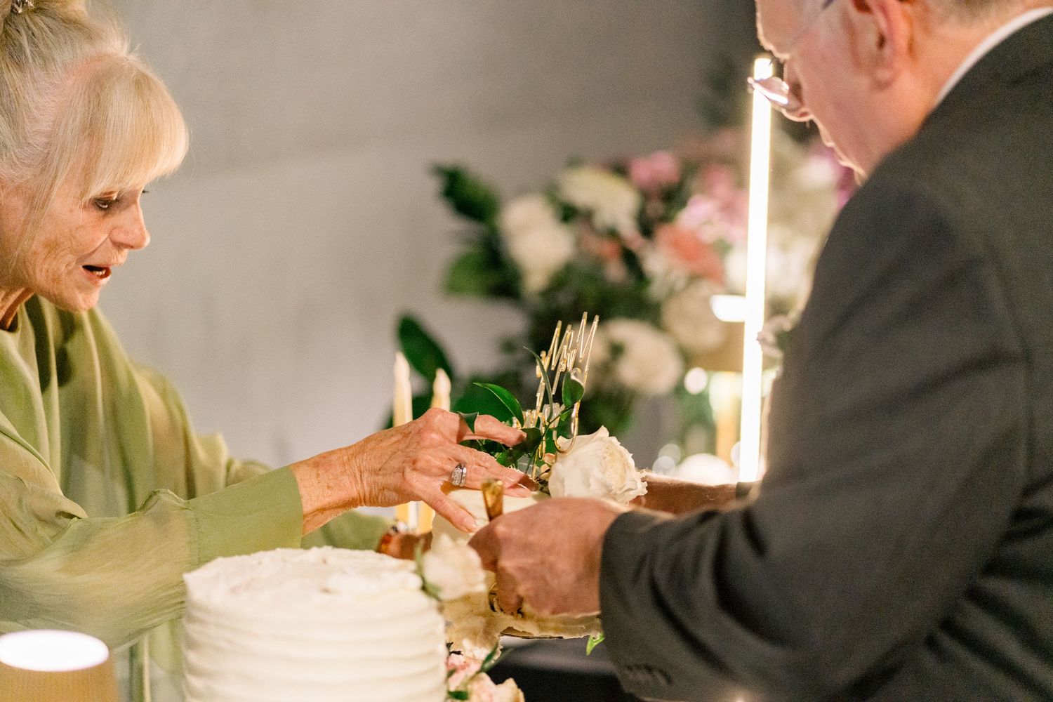 Elderly couple cutting white wedding anniversary cake together at elegant celebration.