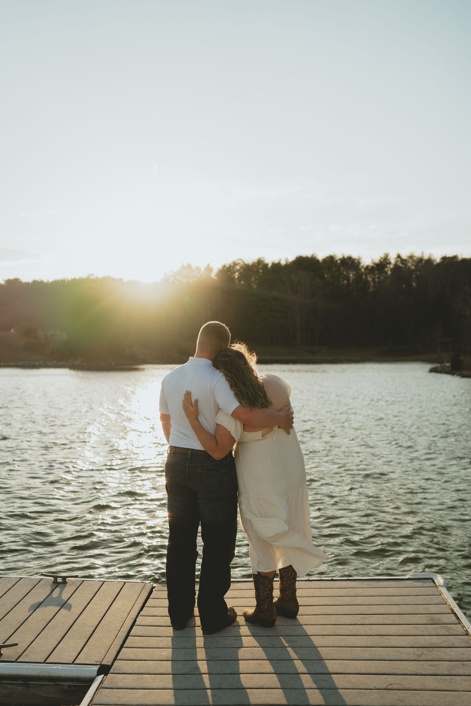 Couple holding each other on a wooden dock watching a stunning sunset over a peaceful lake.