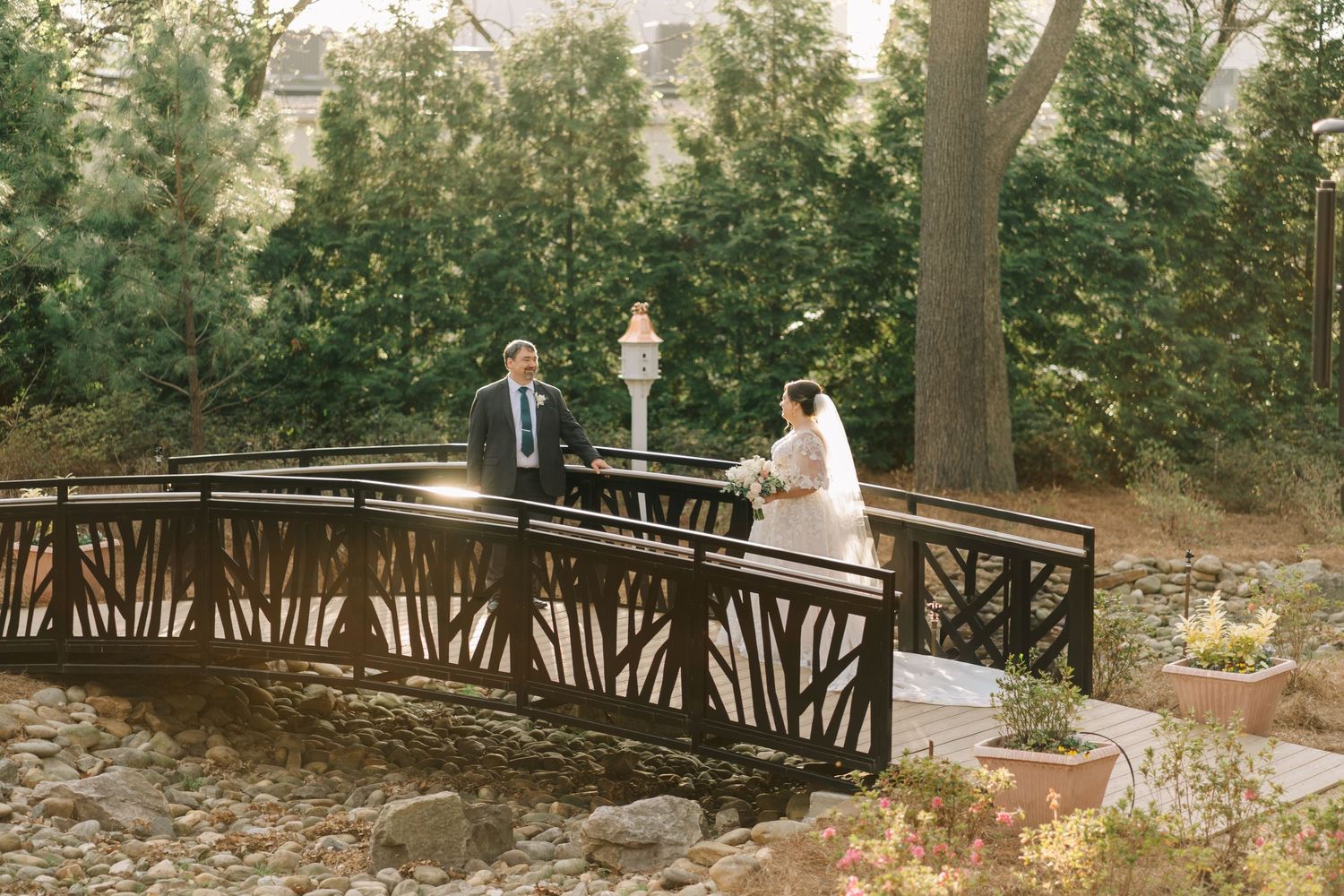 Bride and groom on a wooden bridge surrounded by lush greenery during an outdoor wedding ceremony.