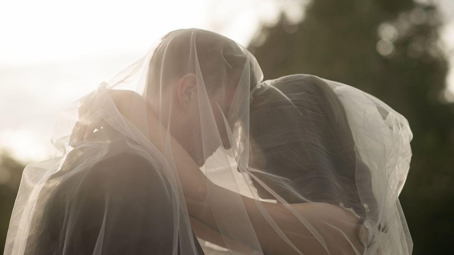 Bride and Groom under veil with a sunset in the background - by Weddings by JACKsBACK Cambridgeshire & Hertfordshire