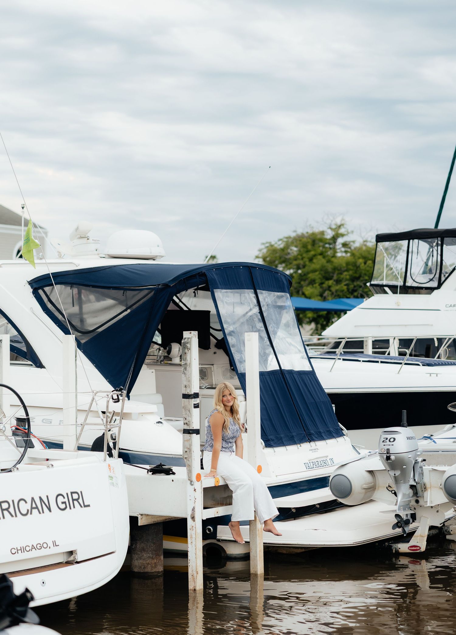 Blonde woman standing on a dock between white yachts at a marina in Chicago, IL on a cloudy day.