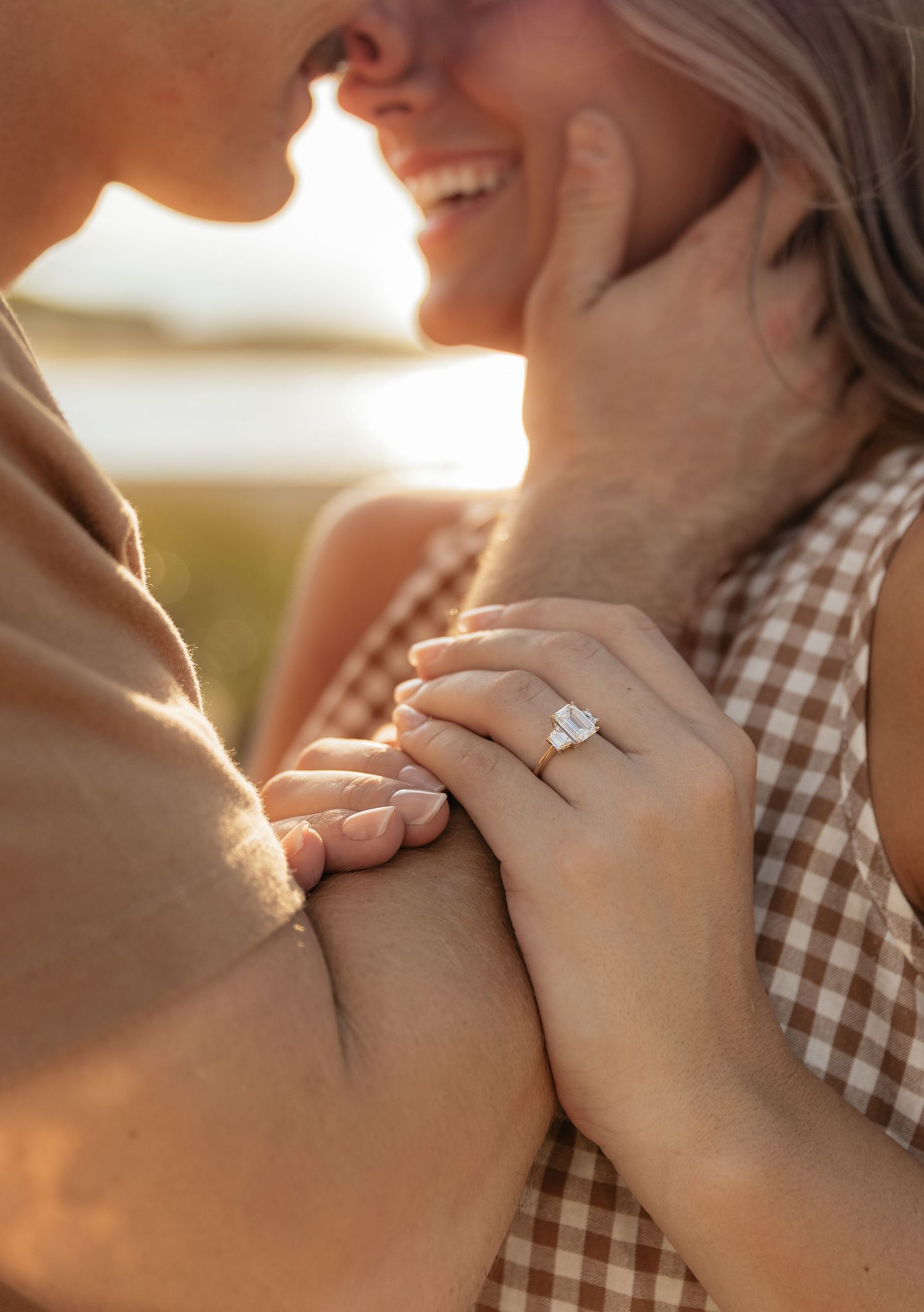 Close-up view of hands holding and caressing during a romantic sunset engagement moment showing a sparkling diamond ring.