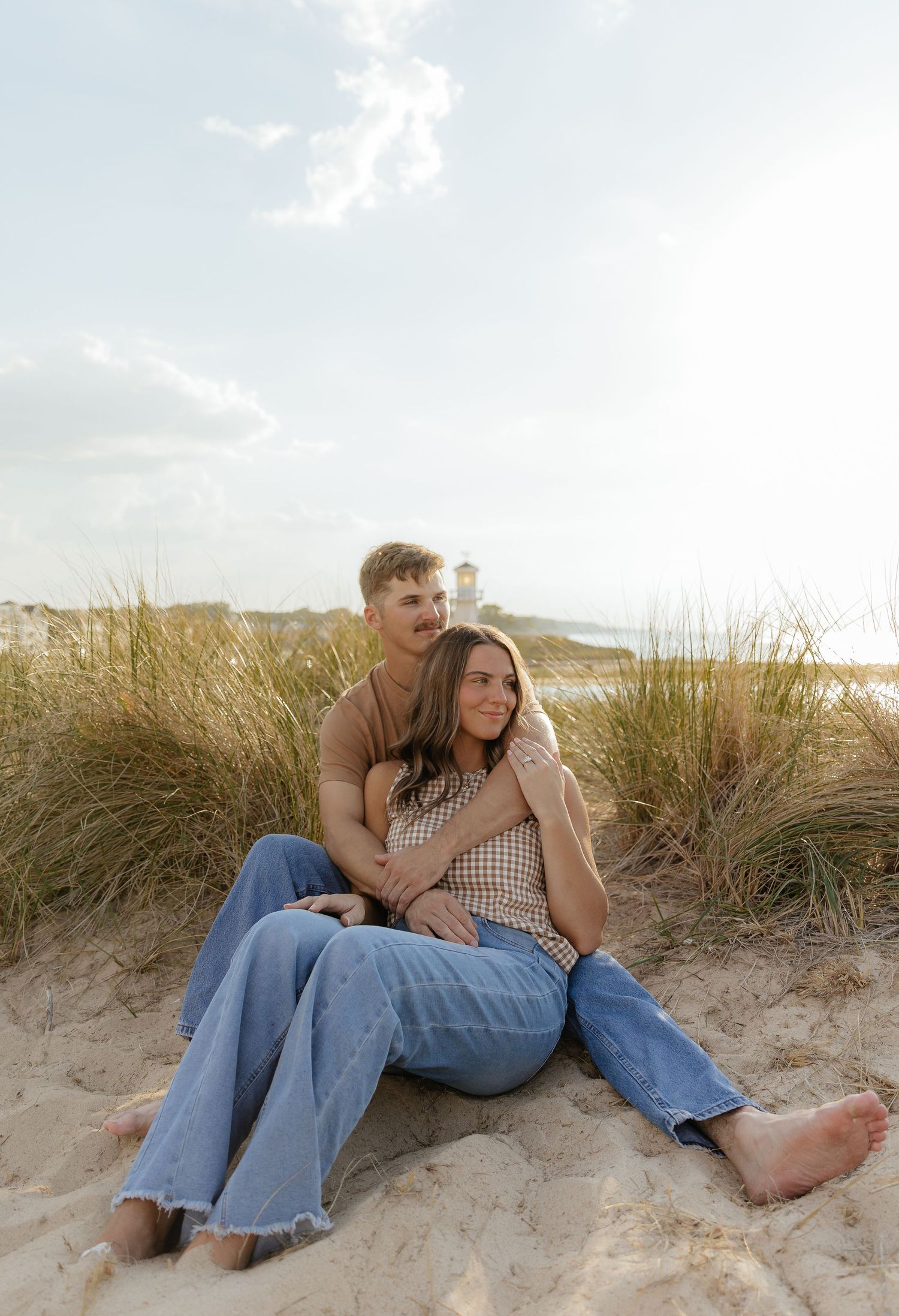 A couple lounges together on a sandy beach with tall grass and dunes in the background.