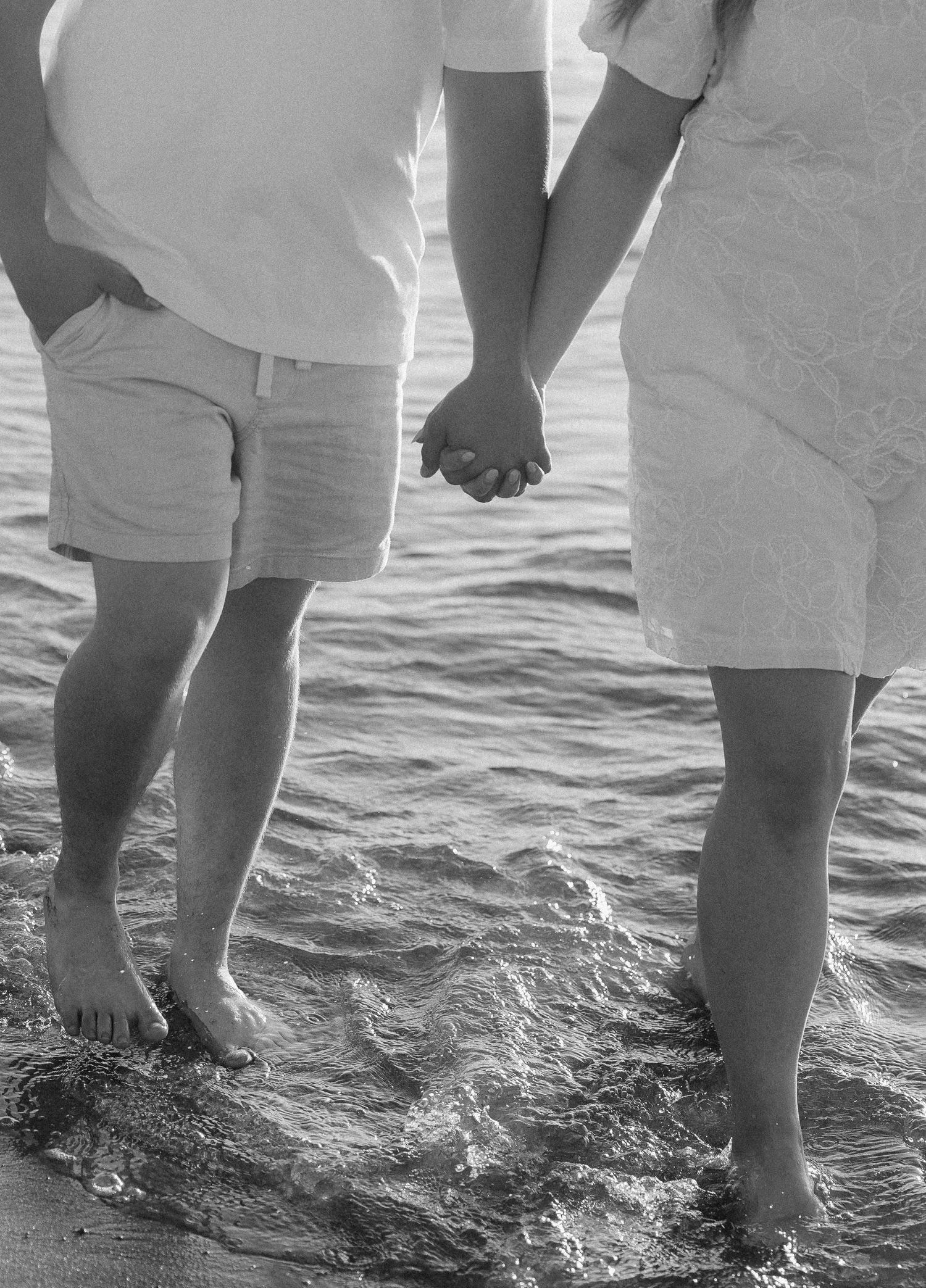 Couple holding hands barefoot at the ocean shore in black and white romantic beach photography.