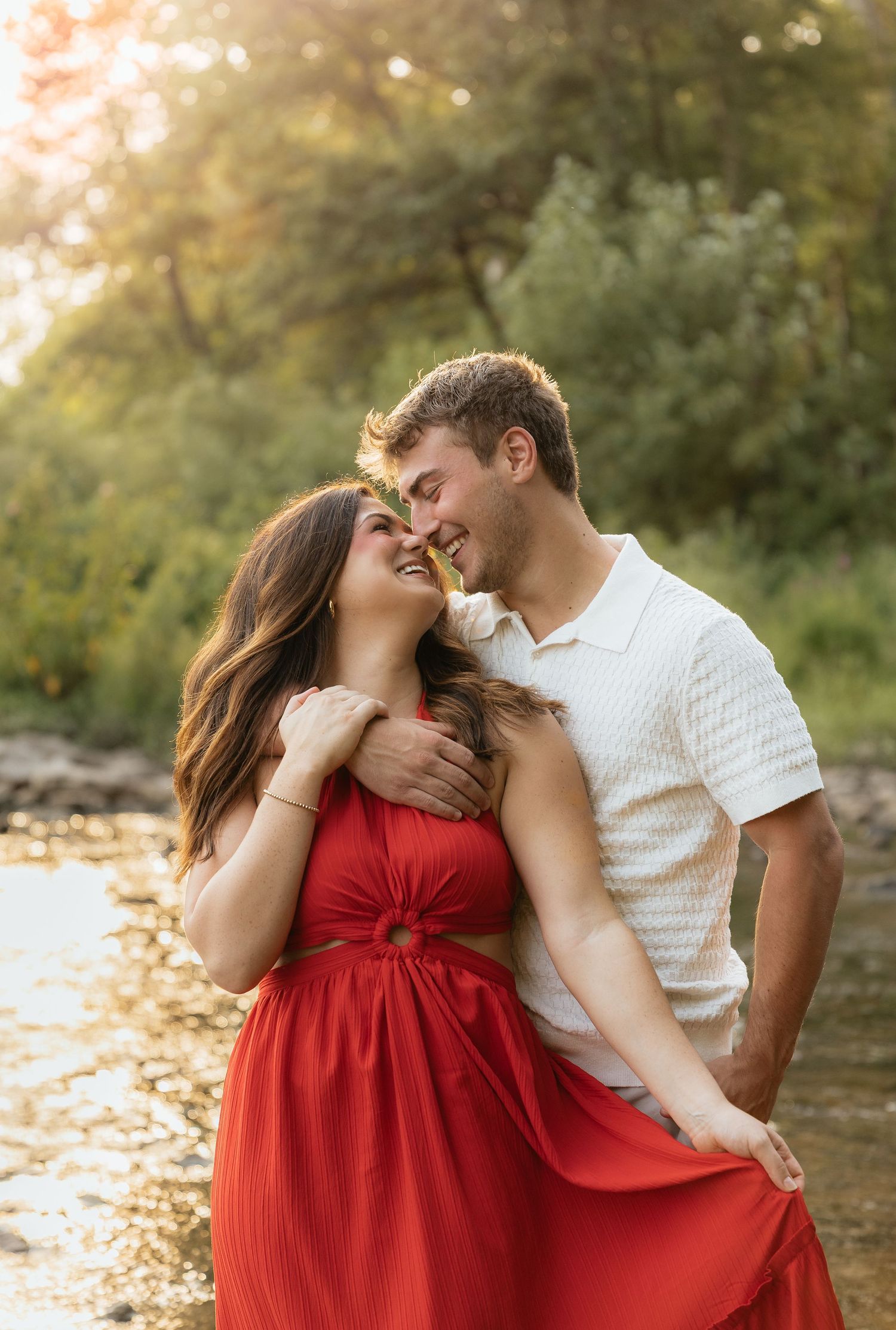 A couple in matching red and white outfits share intimate moments during a romantic sunset photo session outdoors.
