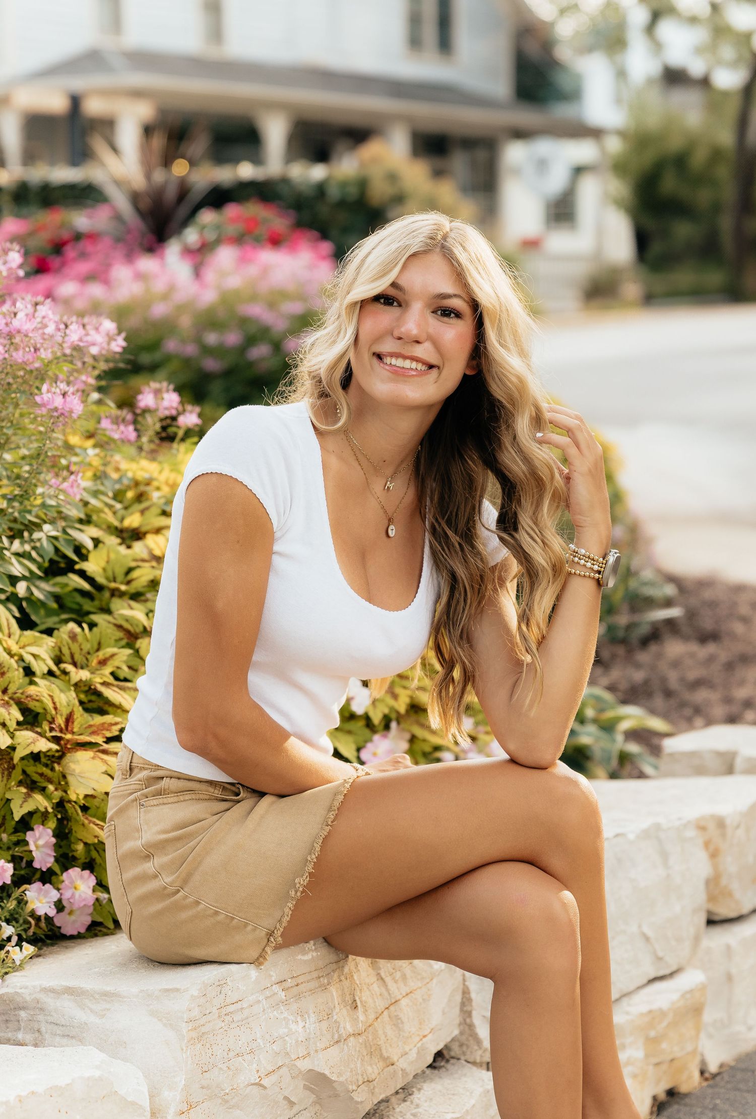 A casual summer outdoor photoshoot featuring a person in a white tank top and khaki shorts sitting on stone steps.