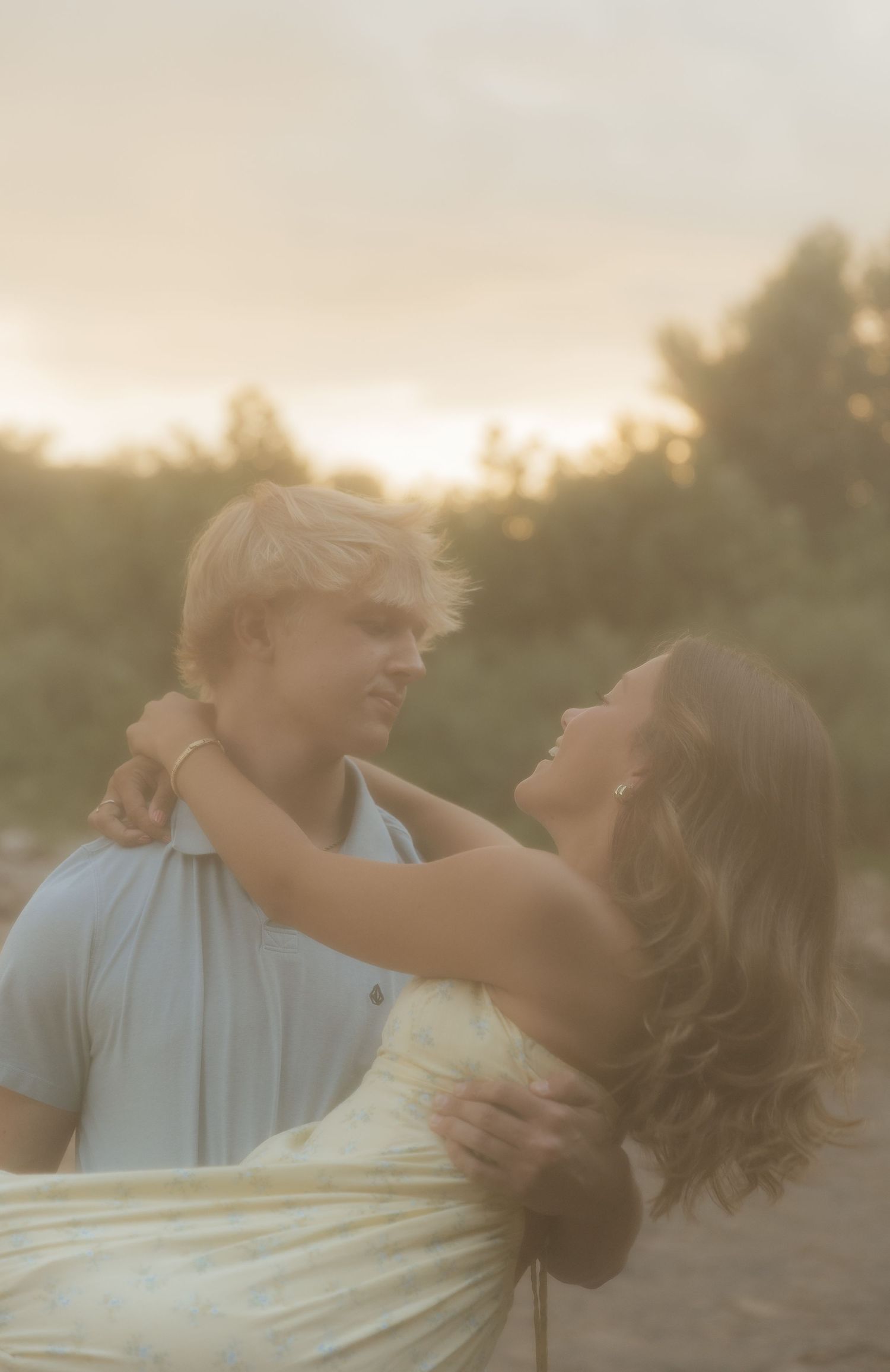 A romantic couple embraces and dances together at sunset in a dreamy golden-hour setting.